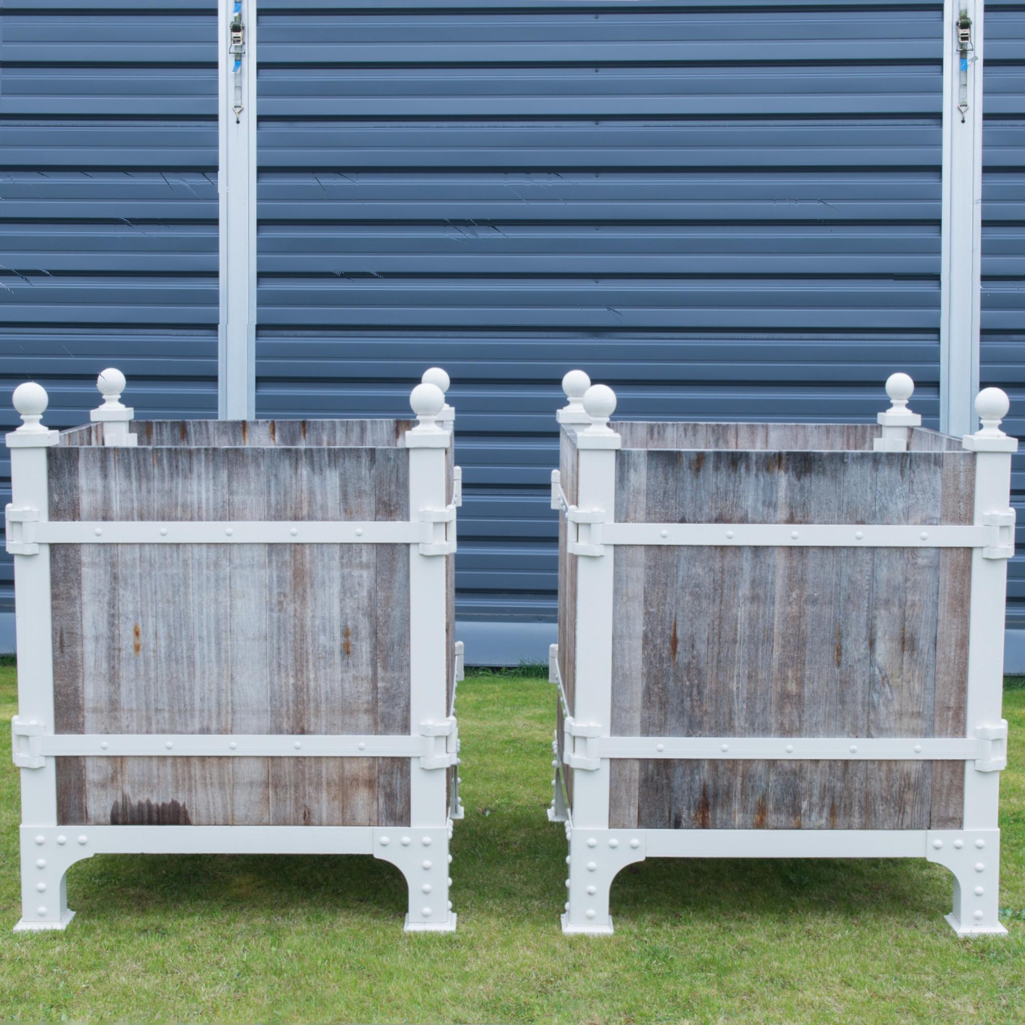 A pair of planters from Poland. A frame of steel girders and rustic wooden boards creates a refined industrial aesthetic. The metal is painted a crisp white, making a striking contrast with the natural finish and muted grey and blue tones of the