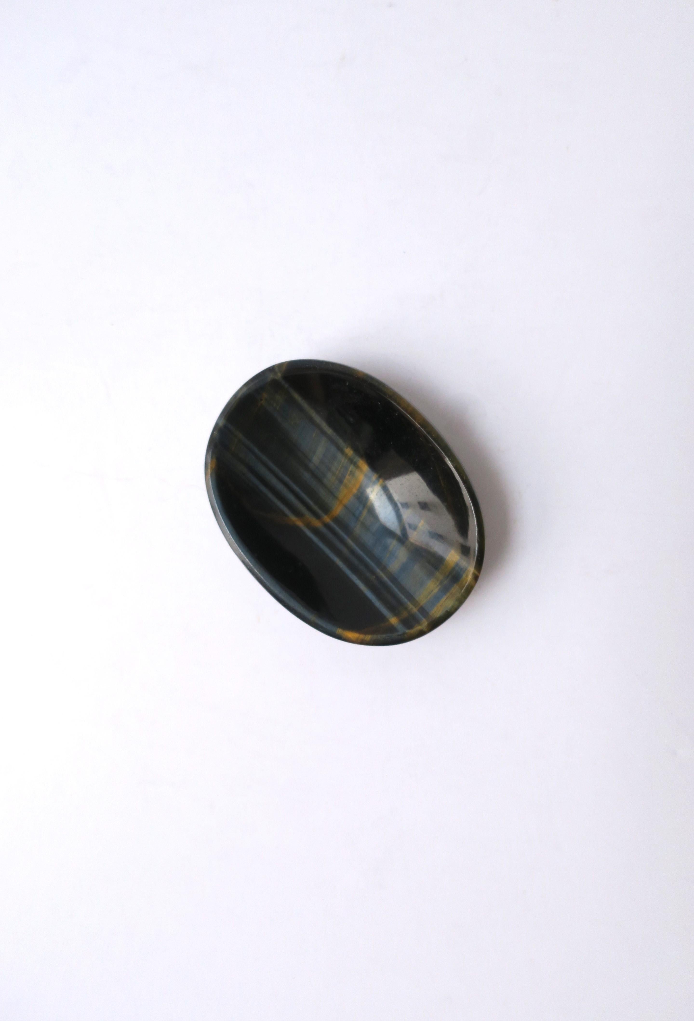A small, oval, polished agate stone dish in a rich dark blue and gold/copper hues, in the Modern/Minimalist styles. Shown holding earrings. A beautiful piece for small items such as earrings, cufflinks, a ring, pills, etc. Excellent condition.