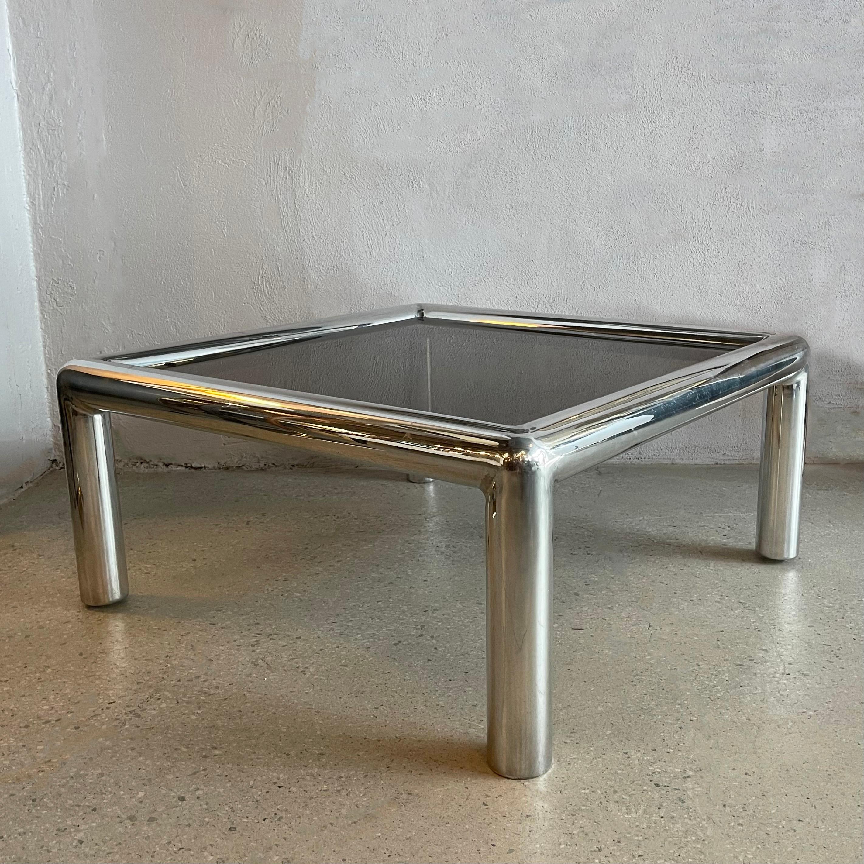 Polished aluminum coffee table known as “Tubo”, by designer John Mascheroni for Vecta, has a seamless design without any visible joinery line. This table includes the original smoked glass top that rest within the frame. The aluminum has a slight