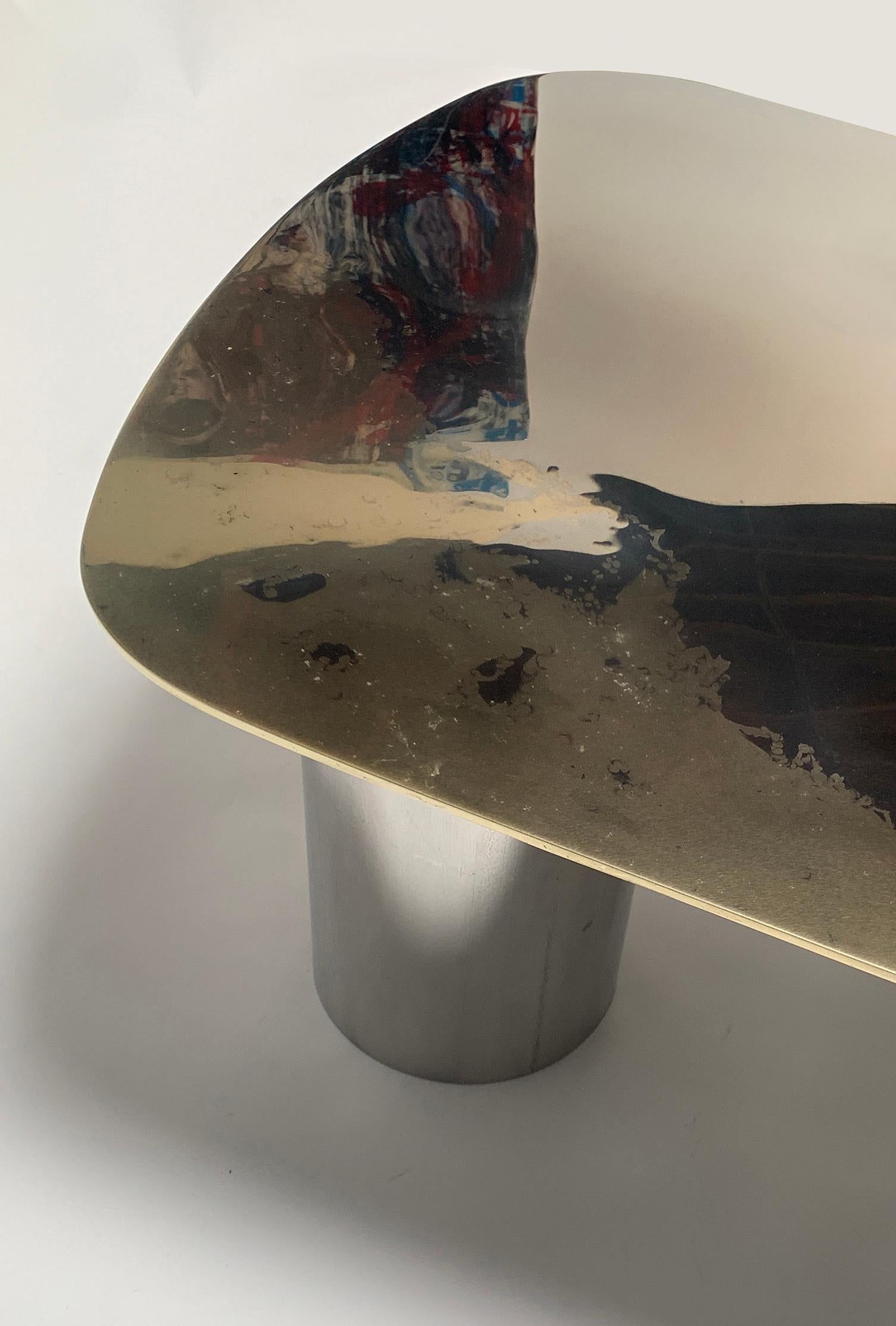 A generous coffee table as part of the Transition collection, featuring an unique, artistic mirror polished tabletop, crafted from brass and stainless steel on tubular bases. 

Studio Warm has developed a distinctive, high-end, artistic finish