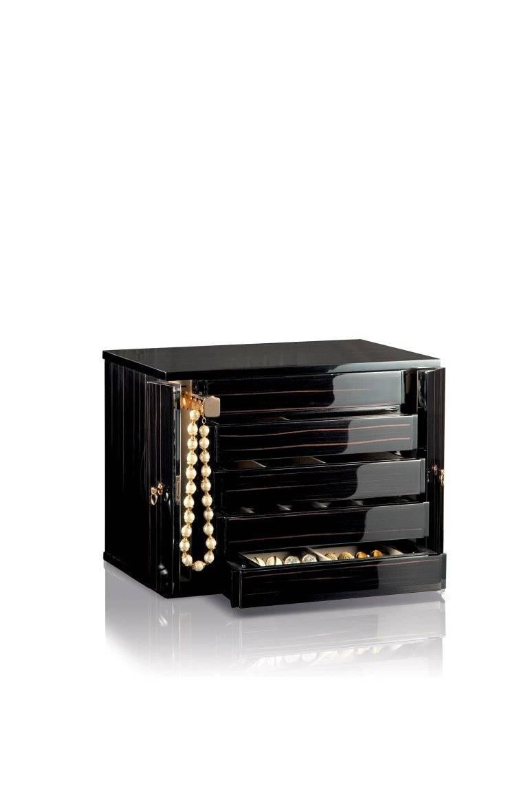 Jewel chest in polished ebony. The two side doors close, by key, the five drawers. And on the side you have two necklace bars. The drawers are organized to contain earrings, ring, bracelets, watches and so on. All the hardware is 24-karat pink