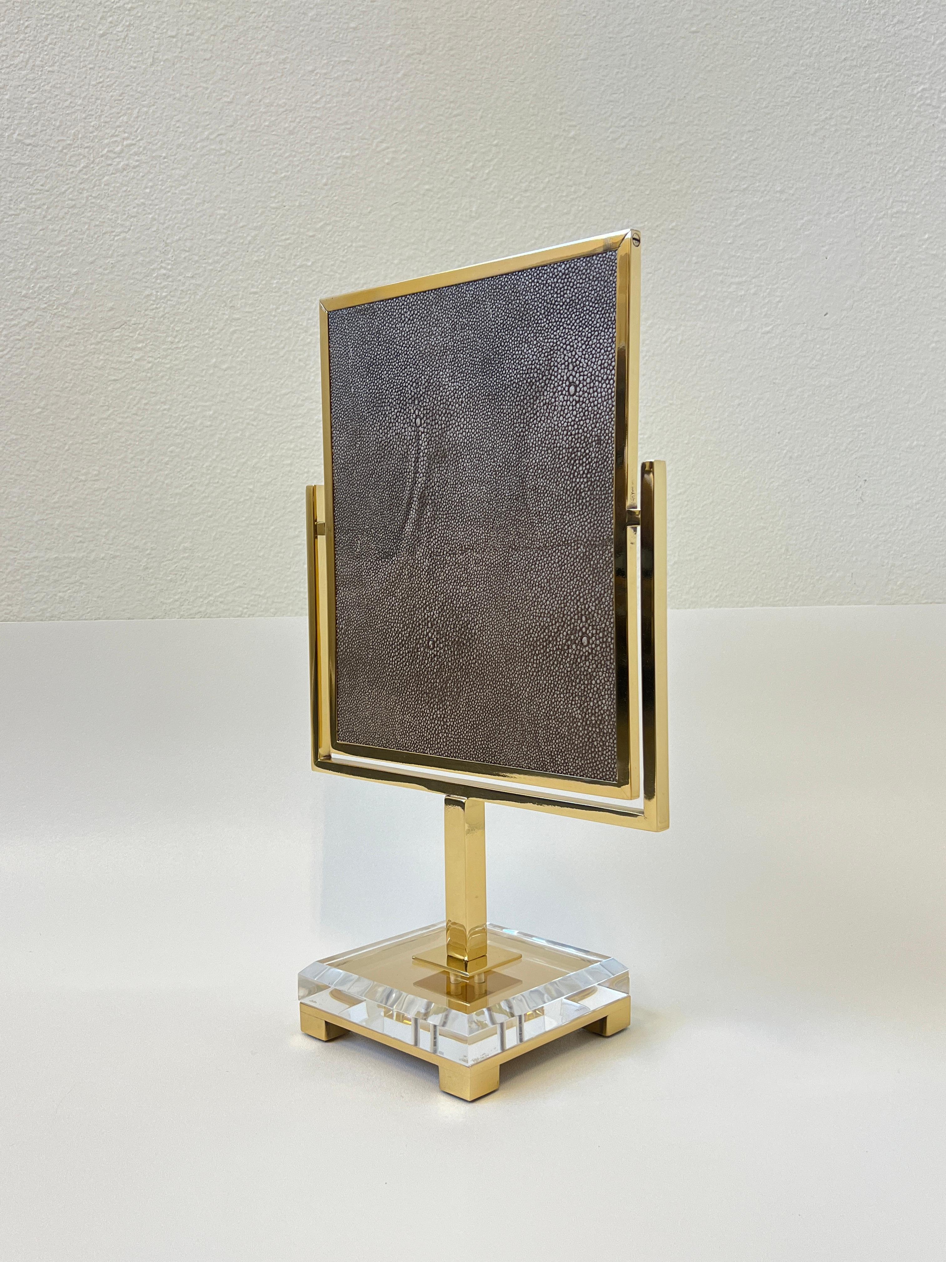 Un miroir de courtoisie glamour en laiton poli et en acrylique transparent par Charles Hollis Jones.
Le miroir est recouvert d'un faux cuir de galuchat brun. Elle a été conçue par Charles dans les années 1970. 
Nouvellement replaqué en finition