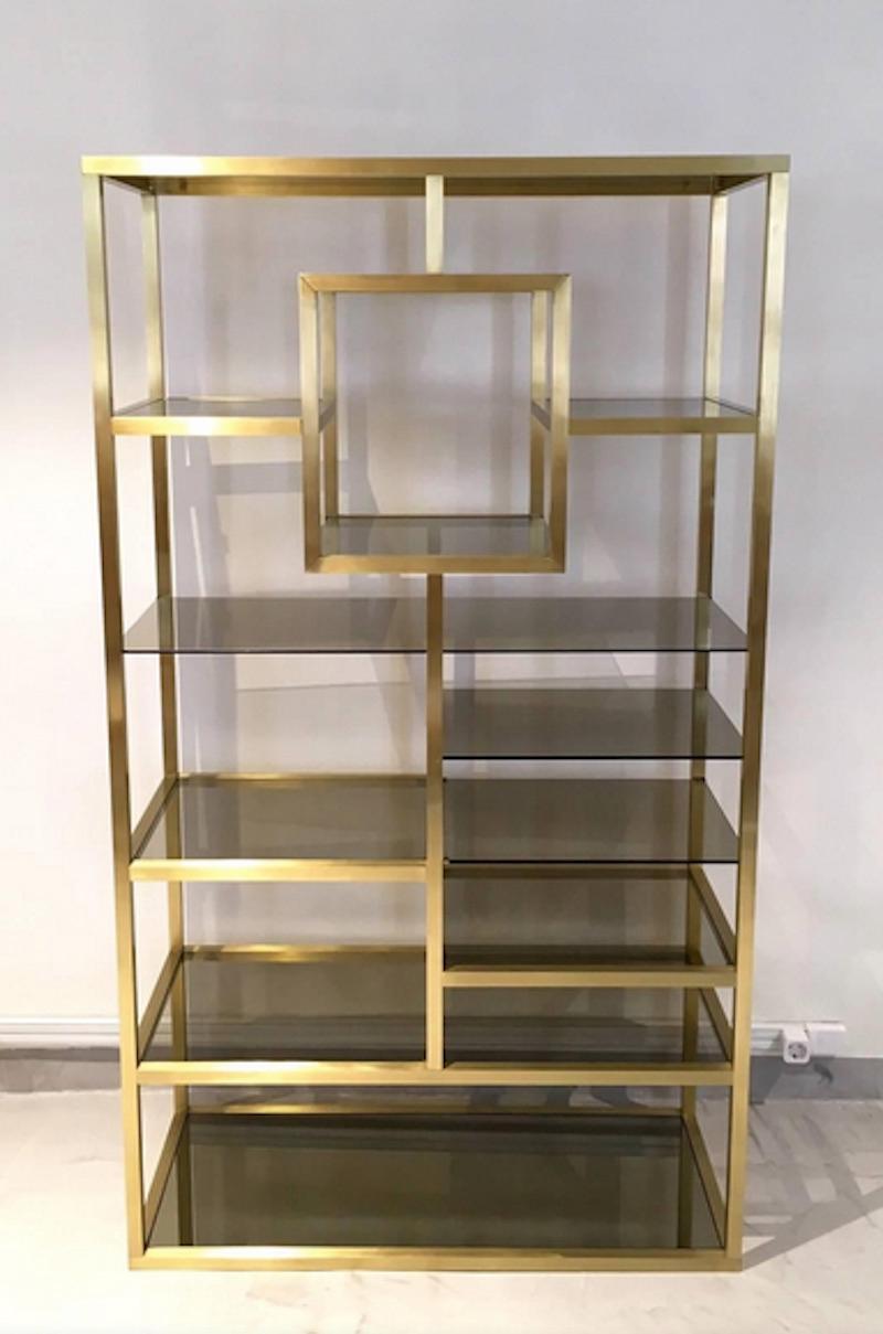 Gorgeous polished brass shelving structure with tinted glass shelves attributed to Romeo Rega. A conversation piece that would look great as a floating room divider. Brass in great restored condition, minor scratches on glass shelves.