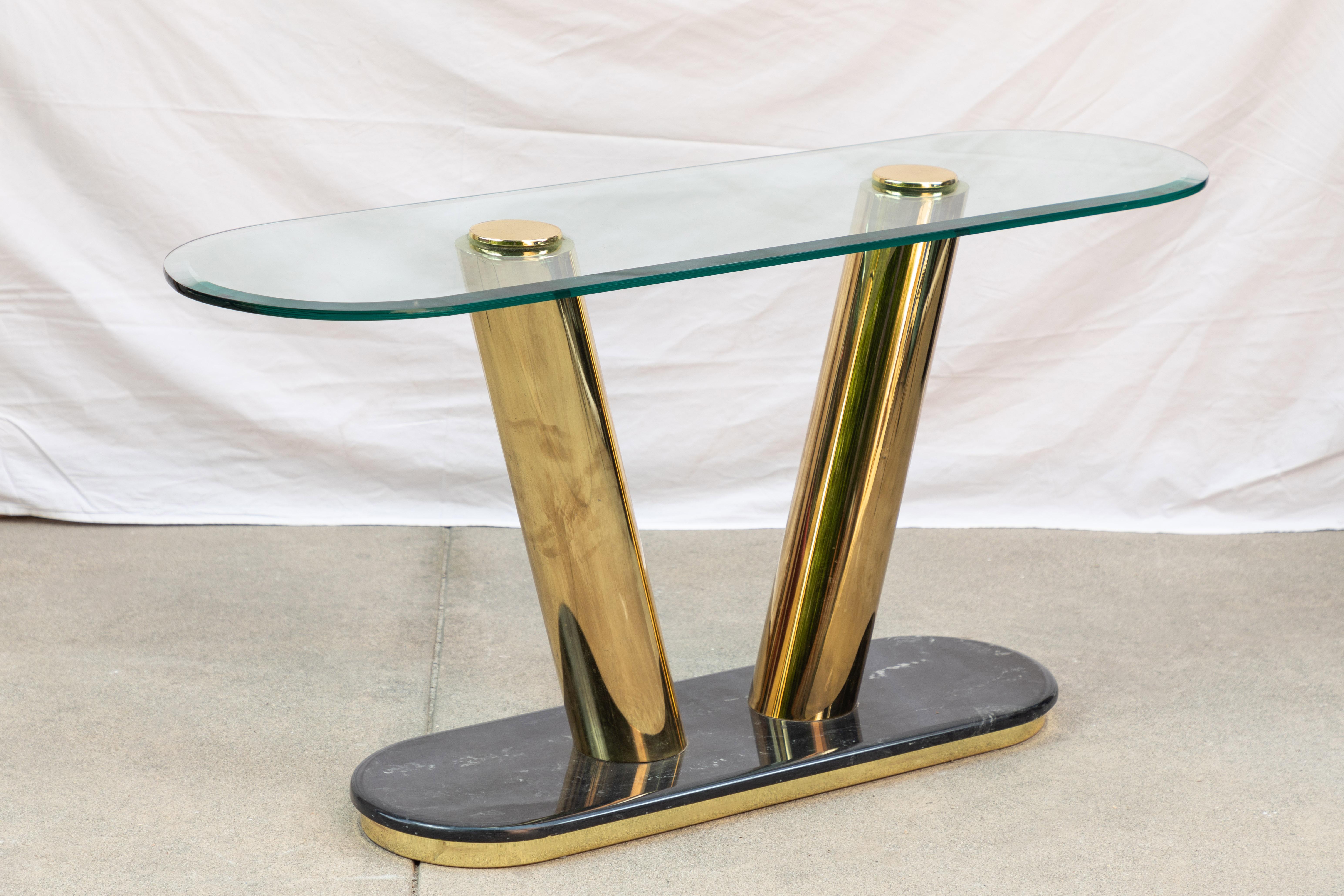 Chic and sleek console table with a glass top supported by two polished brass cylinder legs and sitting on a polished black marble base.