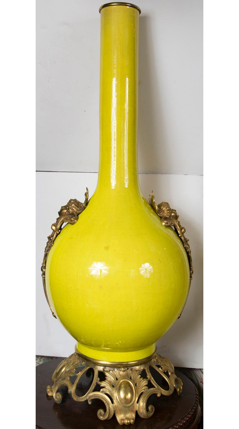 Glazed in a bright yellow with female head masks on either side and a bronze rococo base. Bronze ring above open neck.
The diameter of the base is approximate 15 inches.
The height of 41 inches includes the base.