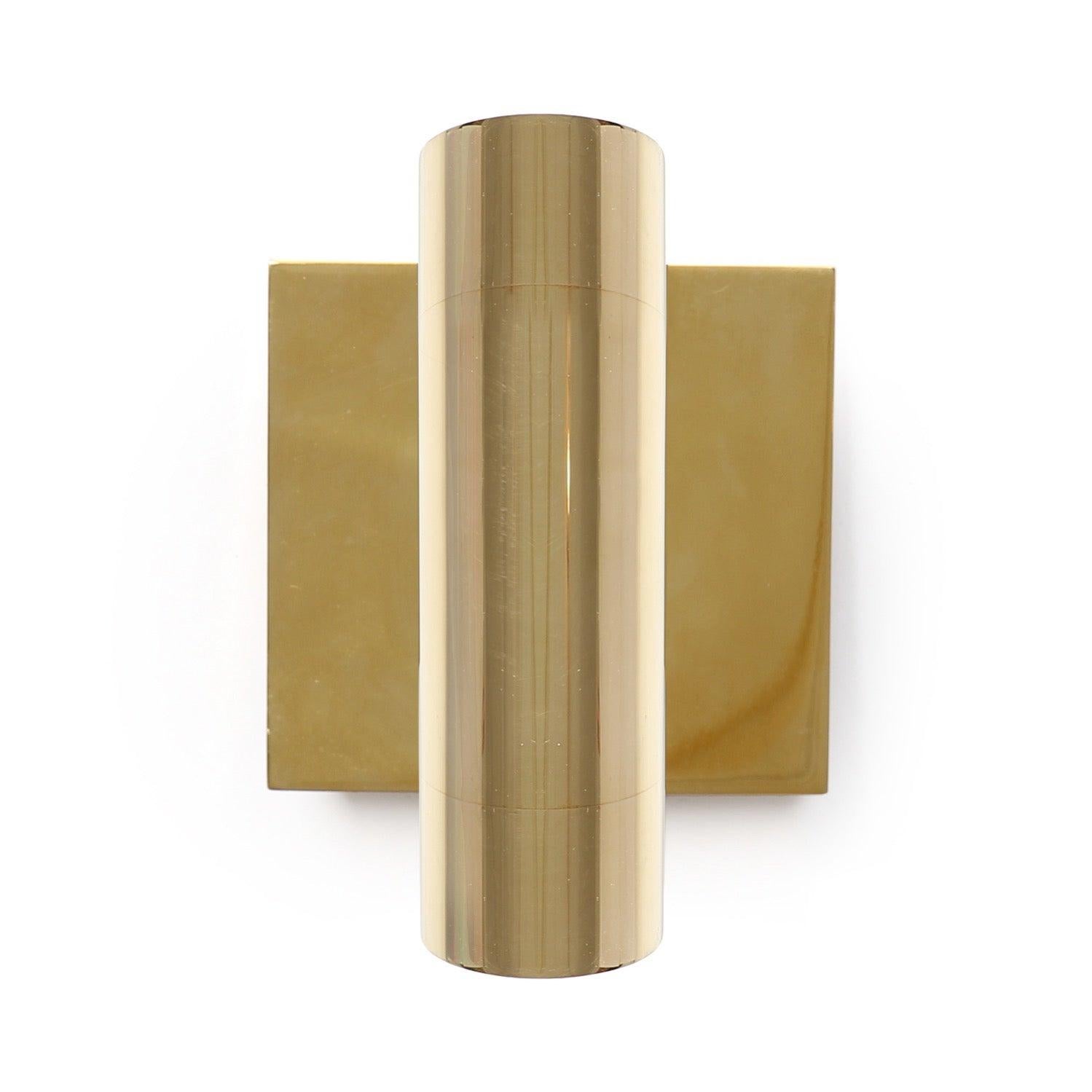 Un'applique minimalista in bronzo lucido di grosso calibro a forma di cilindro che galleggia davanti a una piastra da parete quadrata.