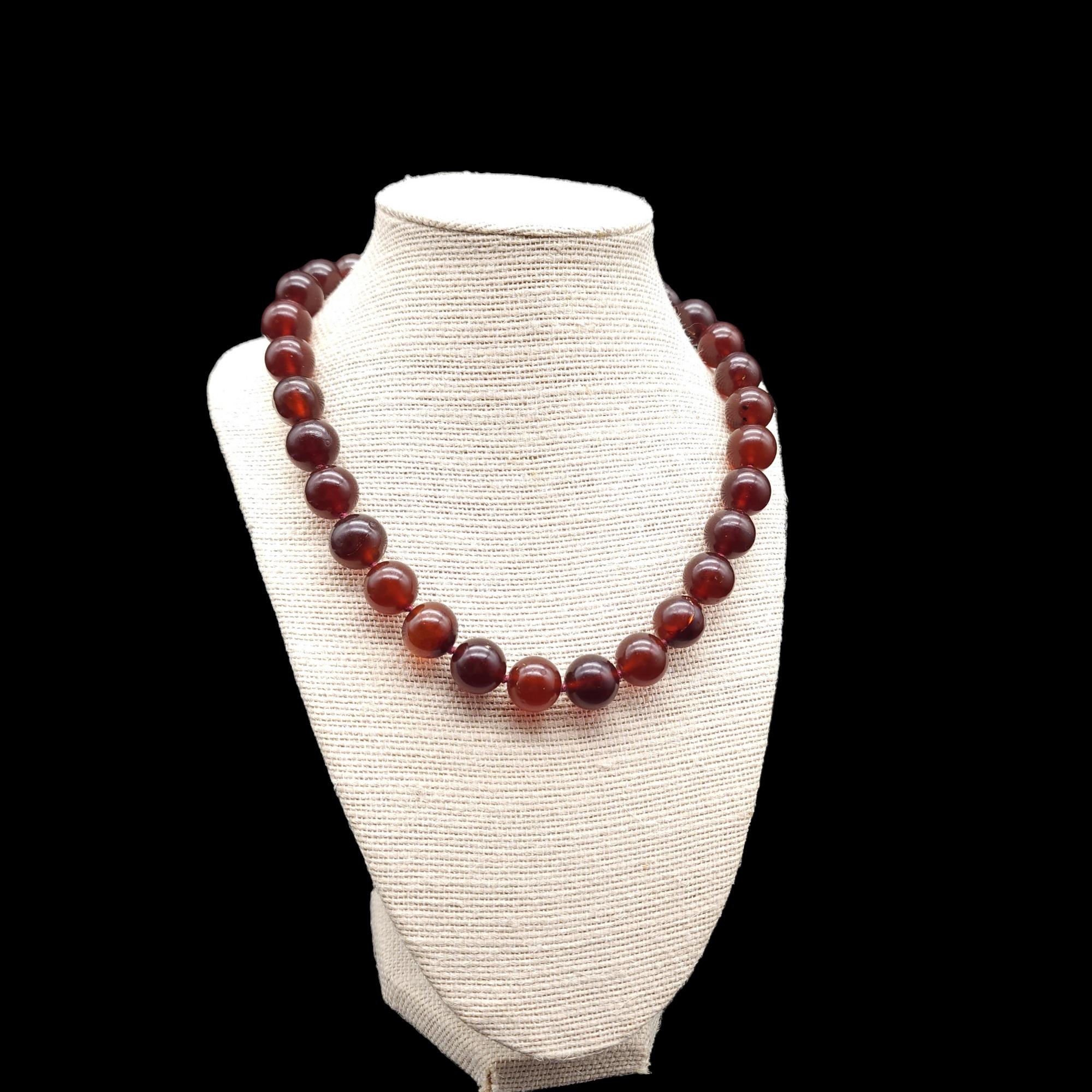 This vintage necklace features polished dark amber beads that have a rich and warm glow. The beads are strung on a sturdy, yet elegant cord with a sterling silver clasp. The necklace has a collar style that hugs the neck. Each amber bead has a