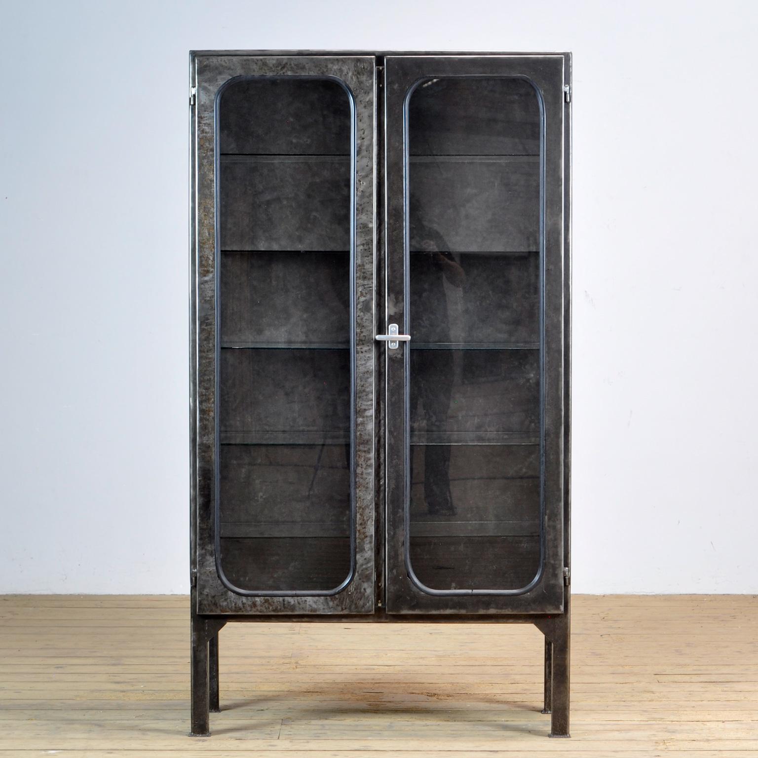 Made of steel and glass that is clamped in the steel by a rubber strip. The cabinet is from the 1970s and was produced in Hungary. The case has been stripped to the metal and finished with a transparent lacquer. The cabinet comes with 5 glass
