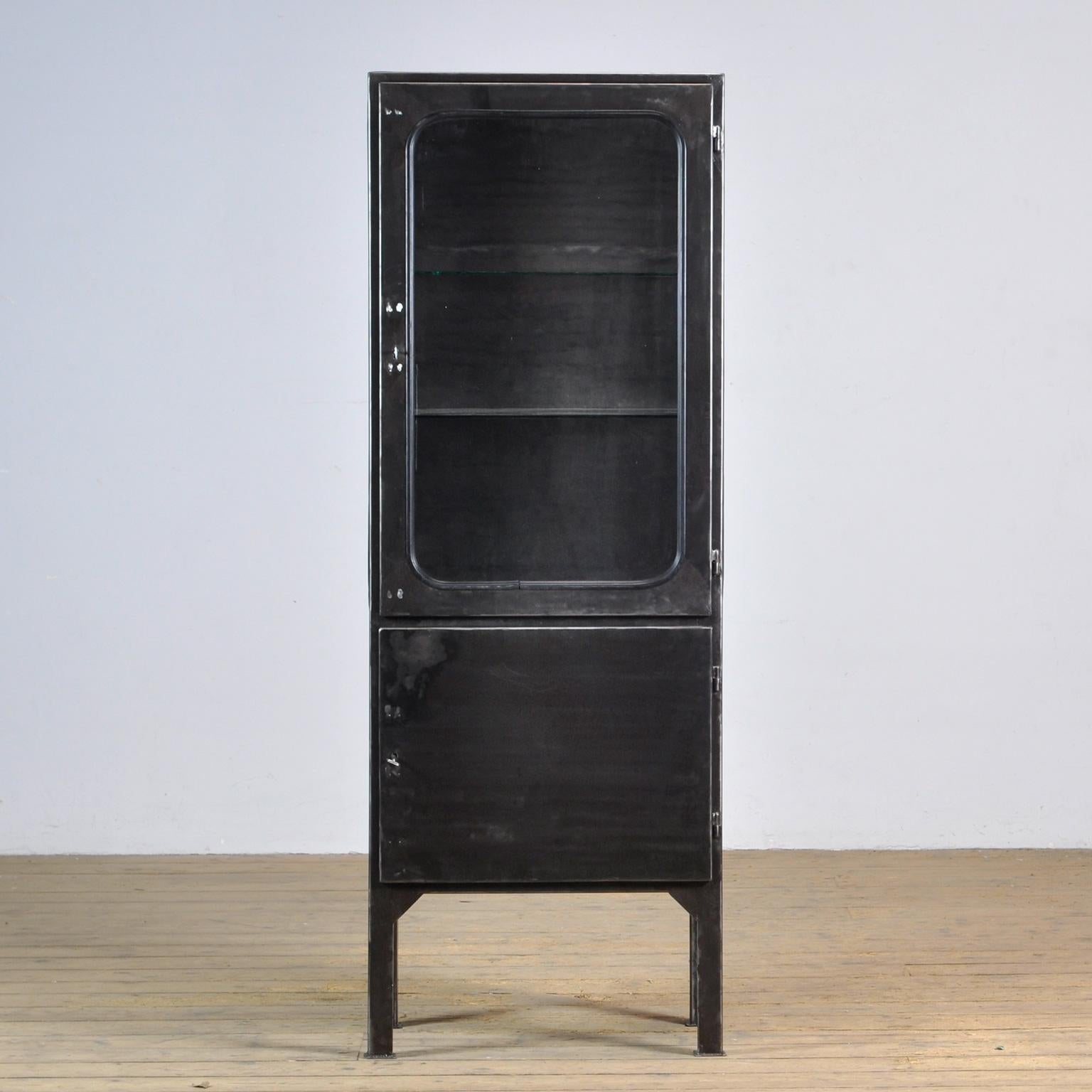 Made of steel and glass that is clamped in the steel by a rubber strip. The cabinet is from the 1970s and was produced in Hungary. The case has been stripped to the metal and finished with a transparent lacquer. The cabinet comes with 2 glass
