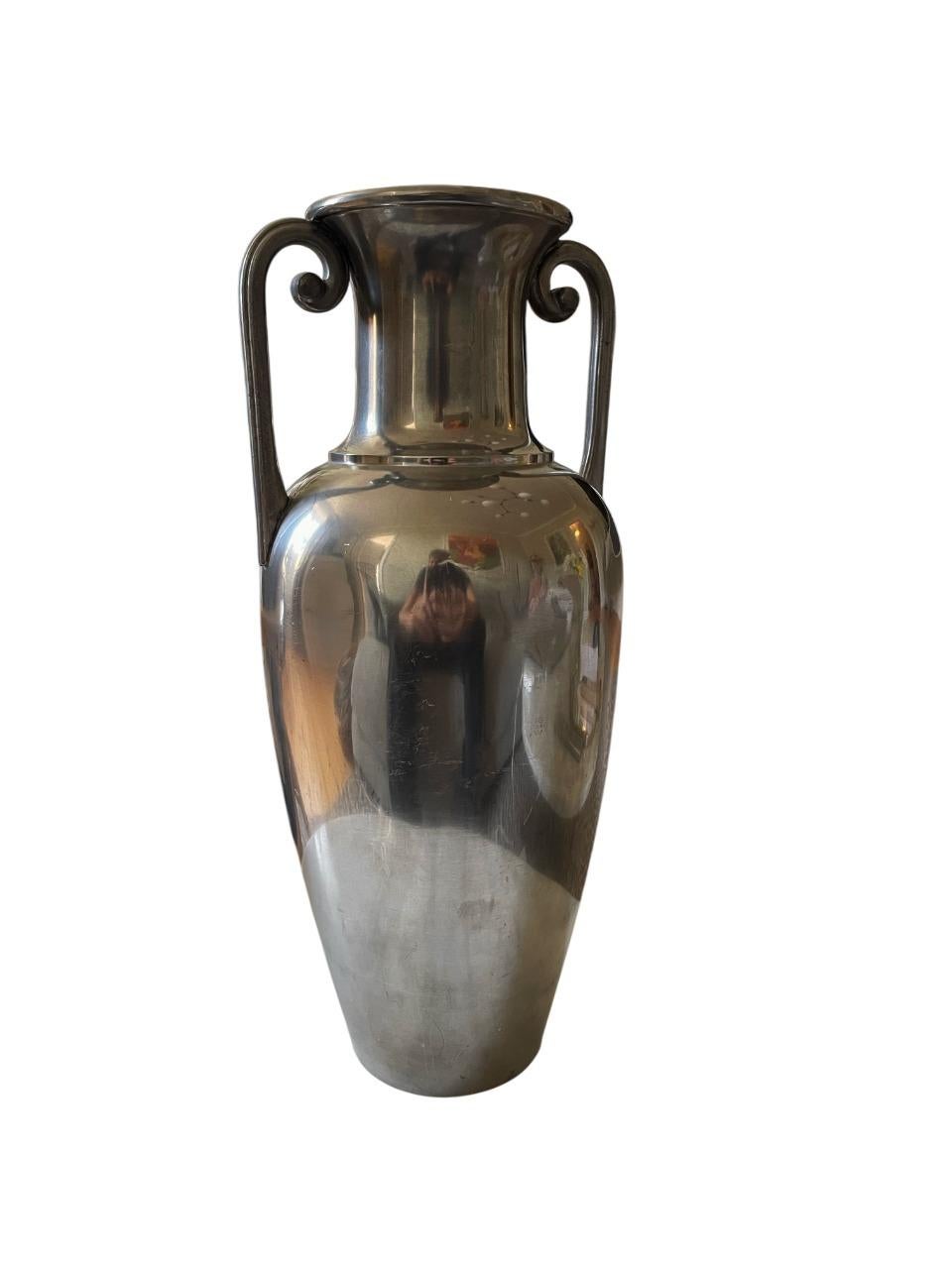 Diese elegante und zeitlose Vase aus poliertem Zinn wurde in den 1930er Jahren von J.L.H.) für das berühmte schwedische Designhaus Svenskt Tenn entworfen. Mit ihren anmutigen Doppelgriffen und dem schlanken, langgestreckten Korpus fängt die Vase die