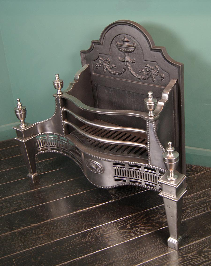 A polished steel dog grate of serpentine form with a fluted pierced apron and central oval paterea. The shaped ornate fire back with urn and harebell wreaths. An Edwardian grate in the Adam manner.  Height of burning area: 9.5