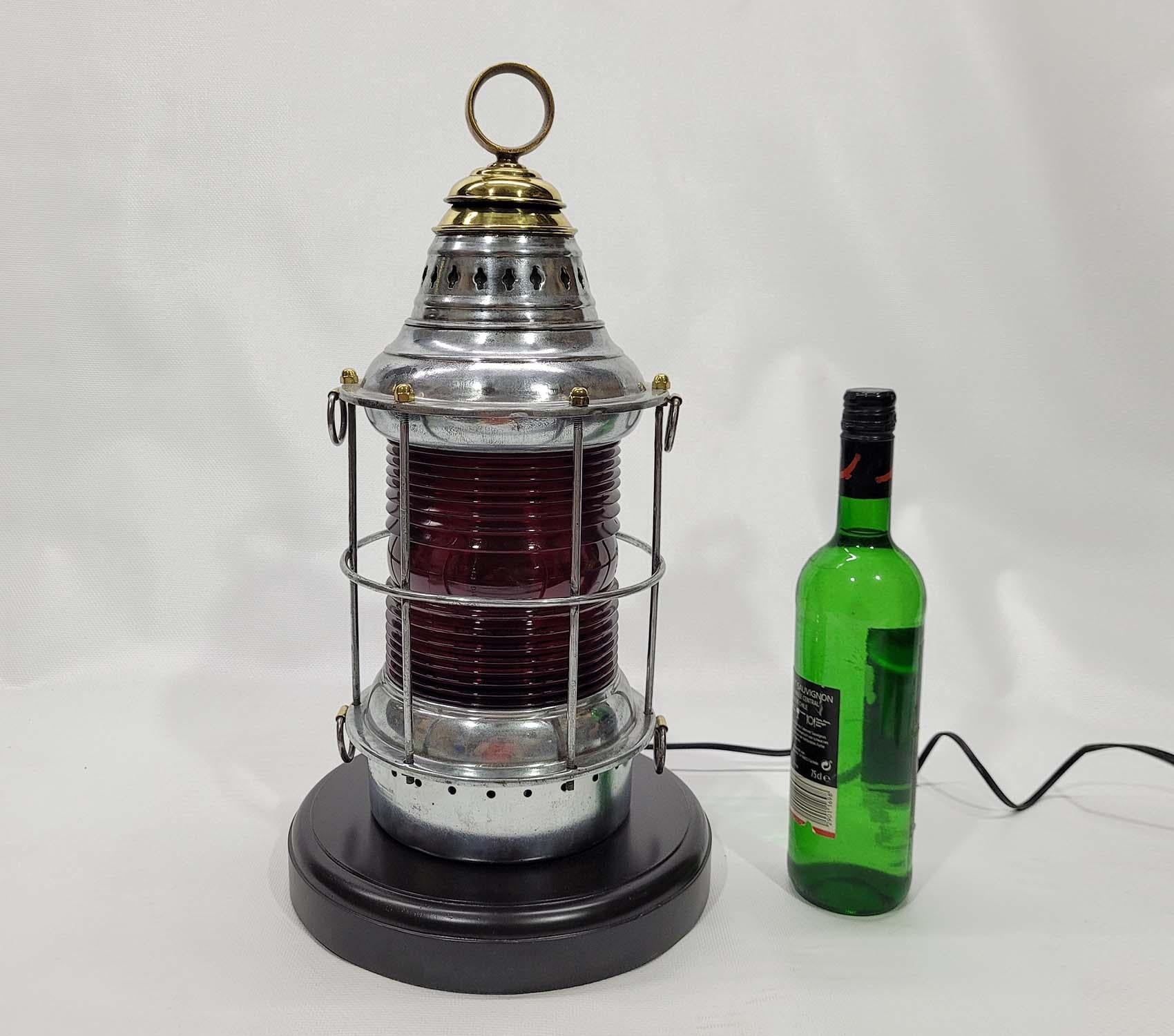 360-degree ships lantern with richly colored red Fresnel lens, protective cage bars, hoisting rings, polished steel case and brass cap. Rewired with a new socket. Mounted to a varnished wood base. This has been meticulously polished and lacquered.