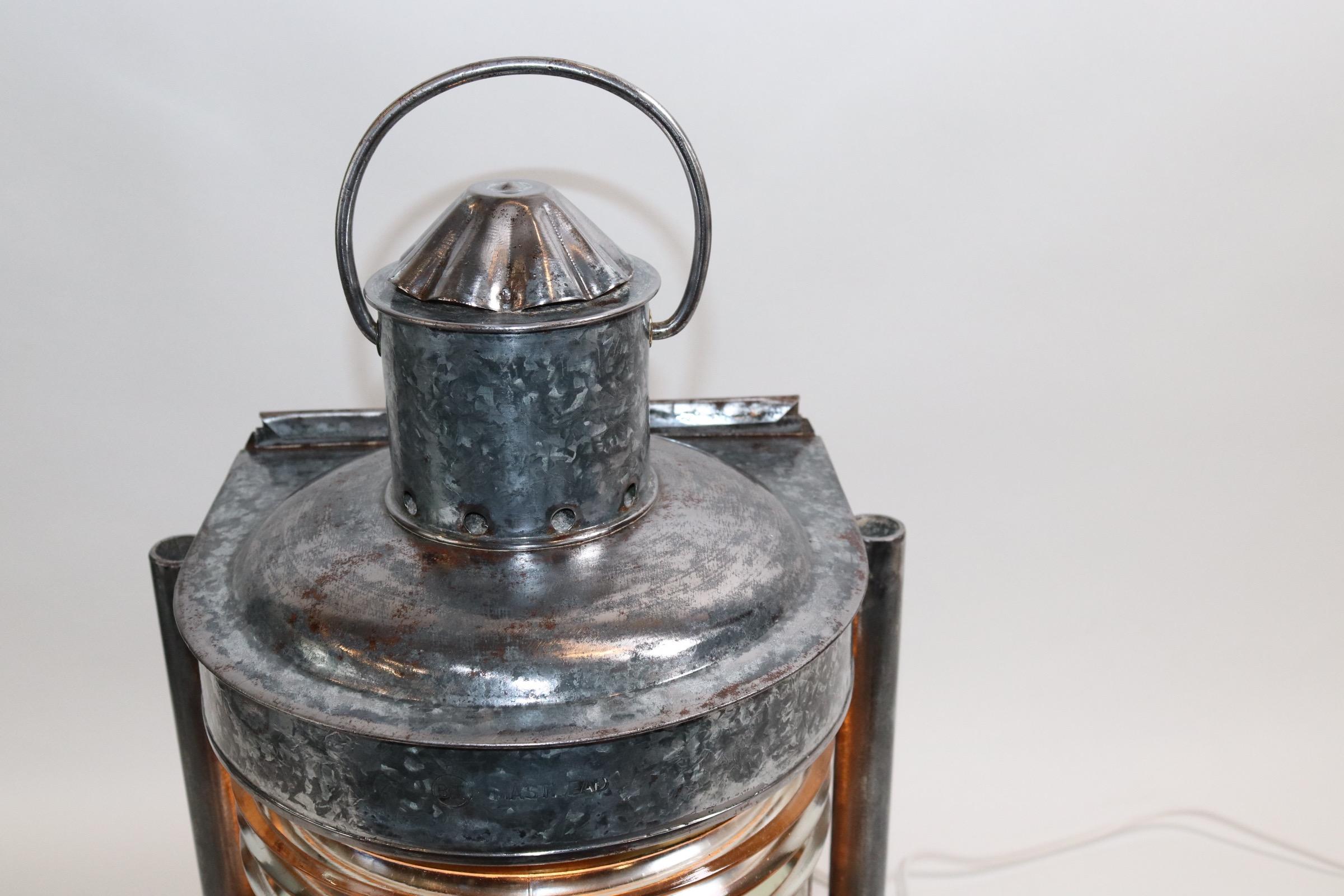 Polished steel ships masthead lantern with clear glass fresnel lens, mounting flanges, vented chimney, carry handle, mounted to a custom made wood base with rich dark finish. Lantern has been electrified for home use. Weight is 17 pounds.