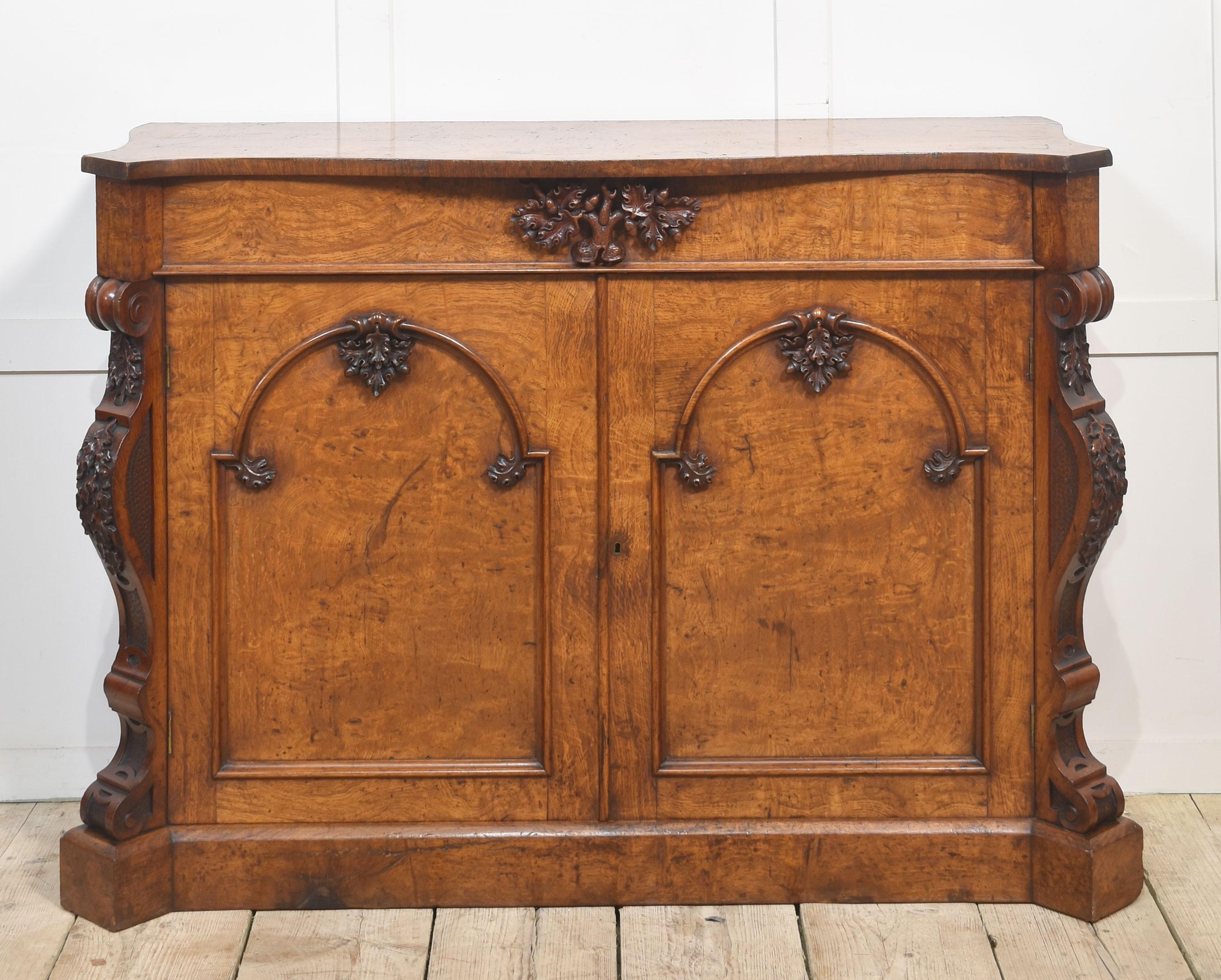 19th century chiffonier, of serpentine outline, having a well figured top, to the freeze fitted with a long drawer with central foliated carving. Above two arched moulded panelled doors opening to reveal large storage area with a single fixed shelf.