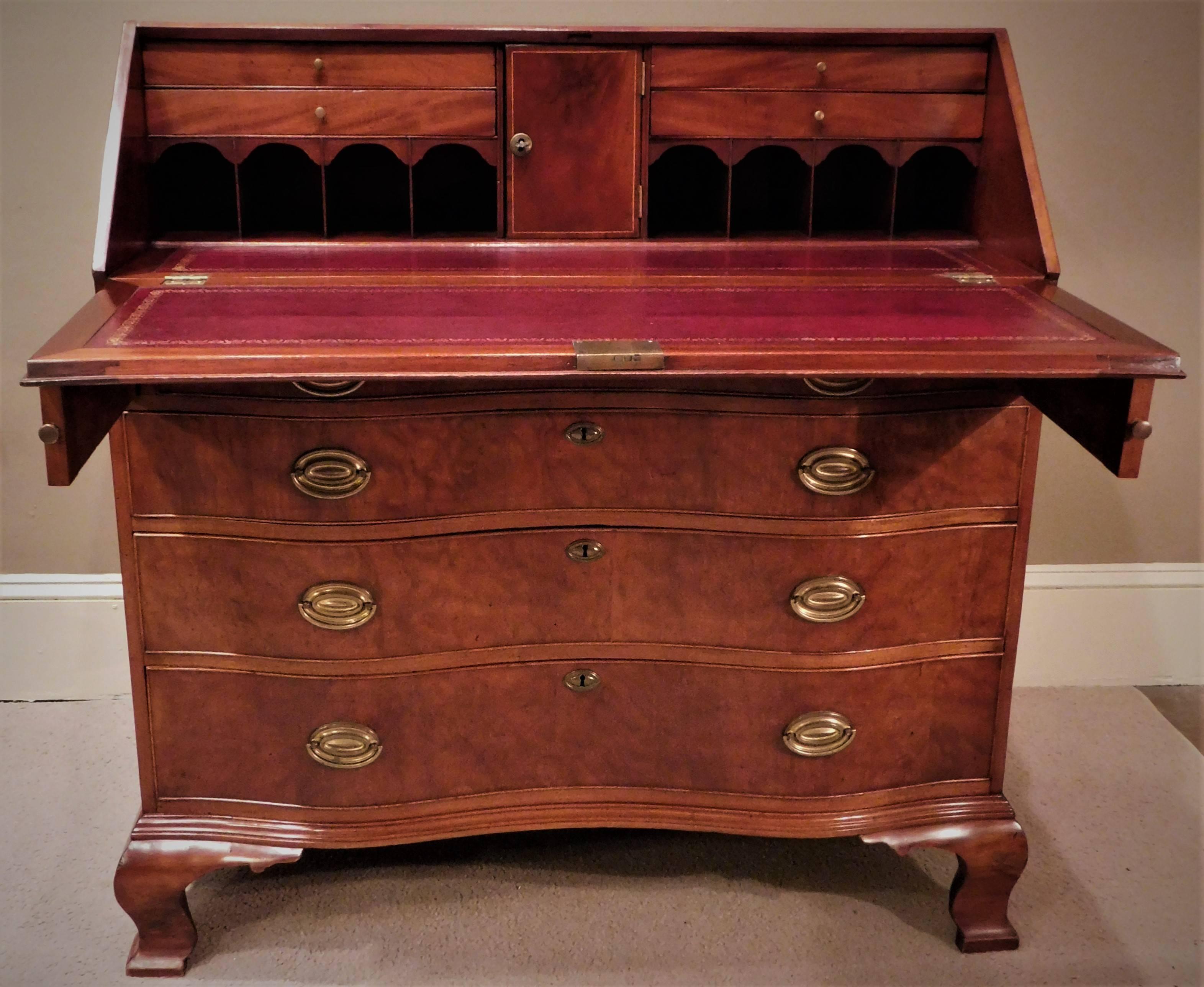 This Georgian slant front desk is made of walnut and pollarded walnut with pine secondary wood and replaced brass Hepplewhite pulls. The desk has a leather writing surface, a fitted interior with six small drawers and one door, over four oxbow