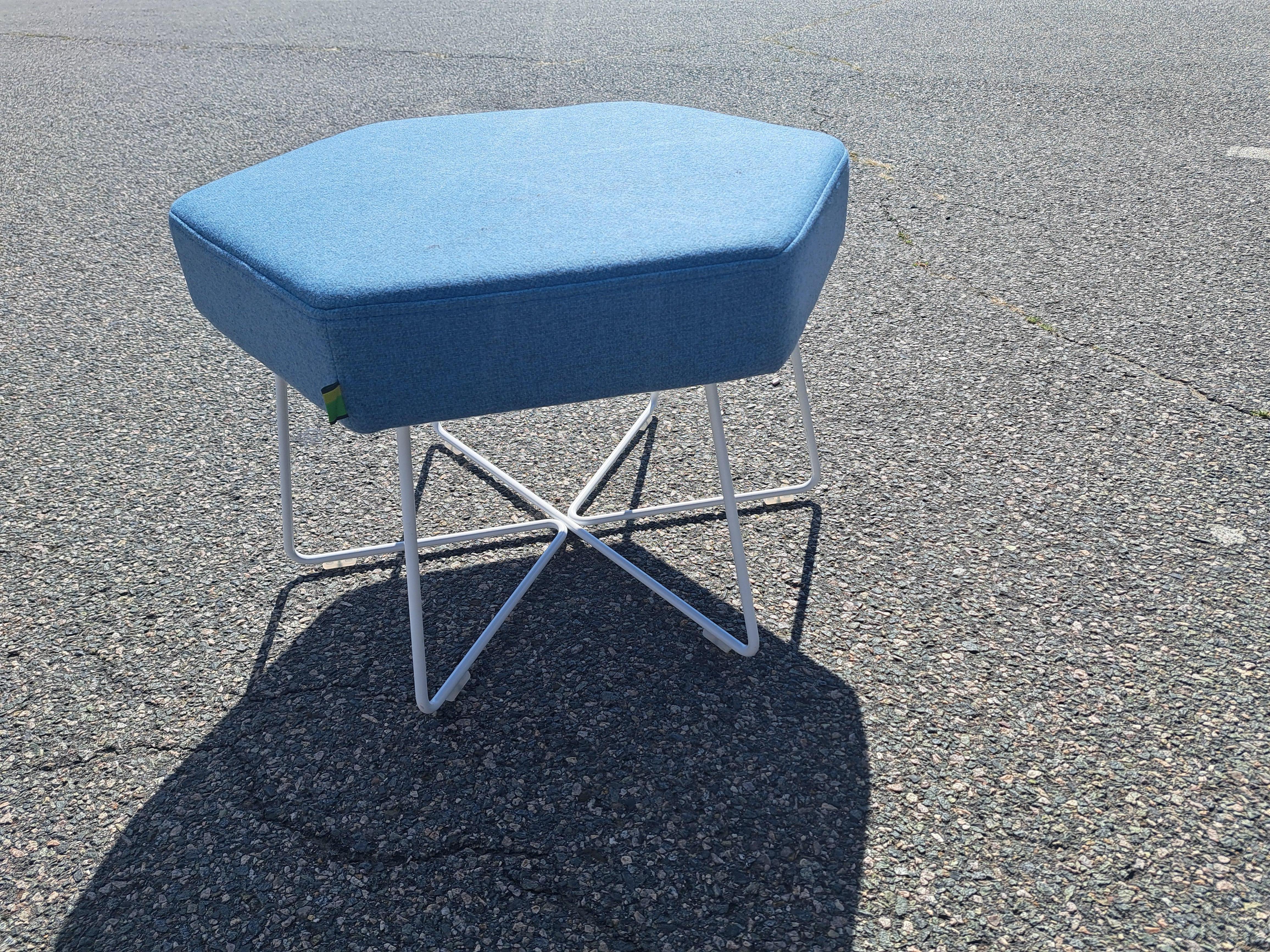 La otomana / reposapiés tiene el asiento acolchado de tela azul polvo con la base cruzada de metal cromado. El artículo tiene forma hexagonal 