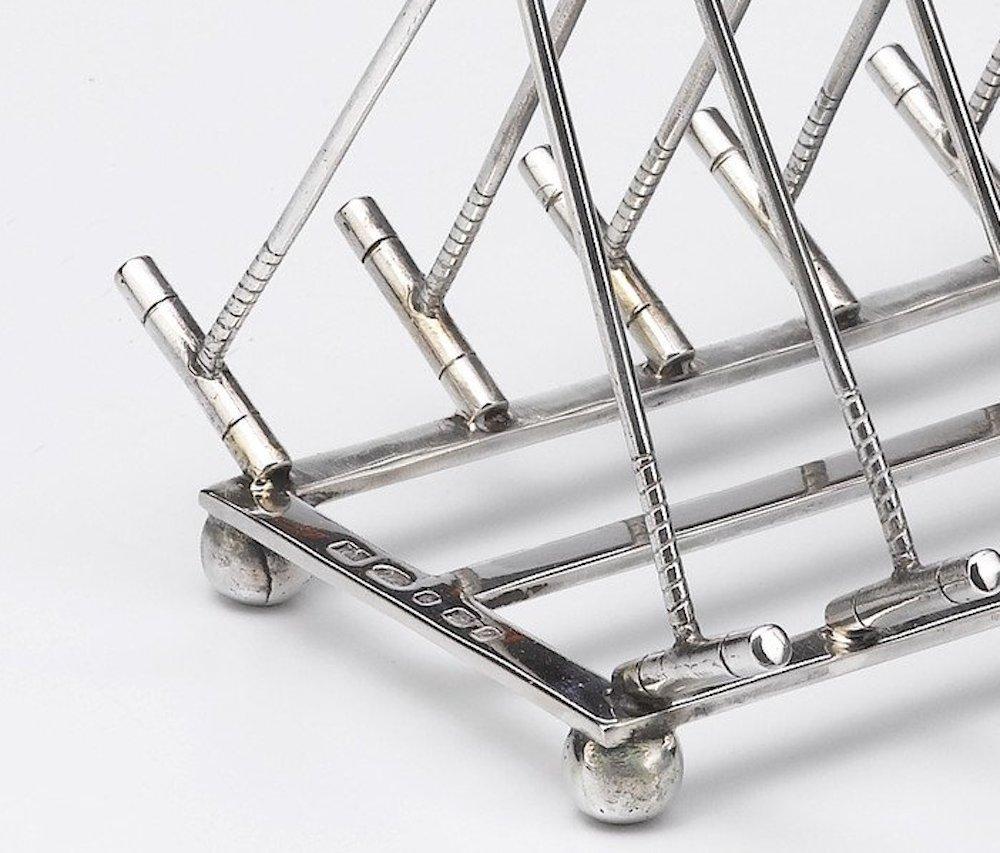 Offered is a beautiful sterling silver toast rack designed with a polo theme. The rack is made up of seven sets of interlocking polo mallets, with a ring handle. The feet of the toast rack are designed as polo balls, to complete the theme. 

A