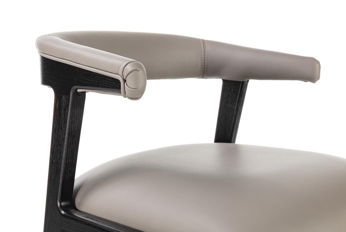 Poltroncina in legno massello dal design essenziale e leggero. Upholstered back with a rounded, wrap-around shape, upholstered in leather. Available in Canaletto walnut or black finish. Seat with fabric, leather or nubuck upholstery.