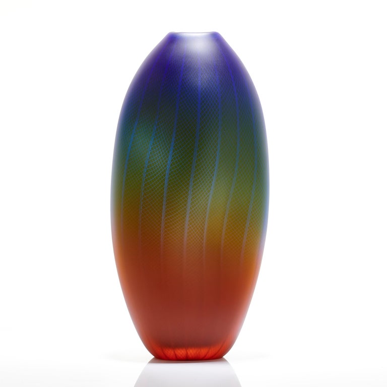 Polychromatic Interleave 004, is a unique handblown glass vessel with fine filigree white cane detail by the British artist Liam Reeves. The three colours of glass in red, blue and green, merge in the making to create a larger spectrum of hues where