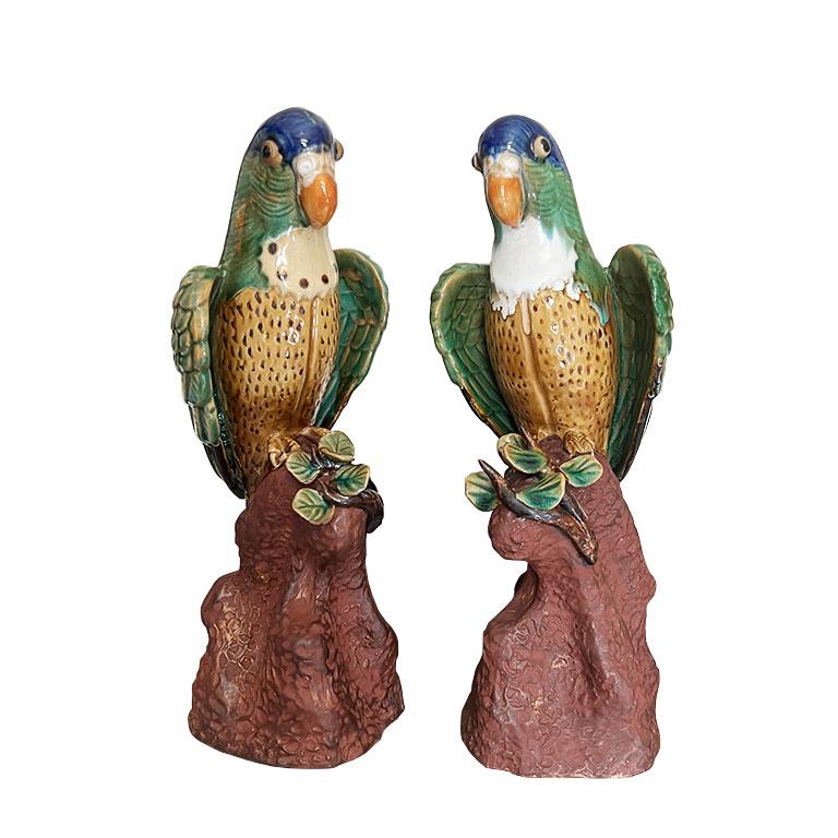 A pair of two ceramic bird figurines in the style of Meissen. Glazed in blue, green, and brown polychrome, this set of parrots will be a wonderful accent to a bookshelf or credenza. Each bird is decorated with a cream breast, with a light brown