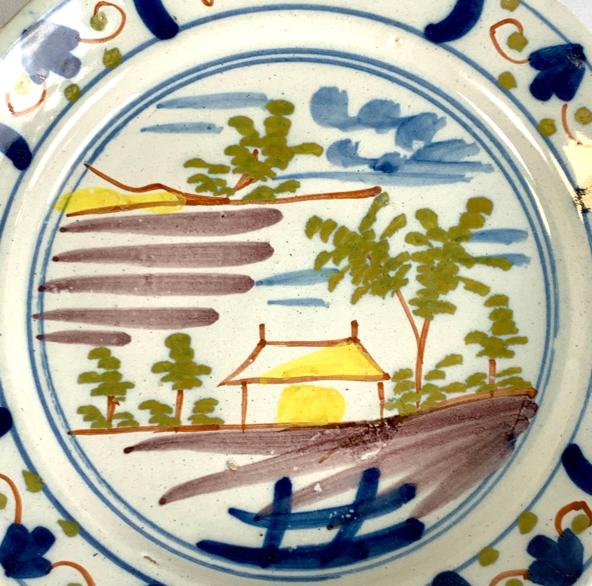 This is an 18th-century Dutch Delft pancake plate hand painted circa 1780.
The artist used the polychrome colors moss green, red, blue, and manganese brown to create a lovely painting of a quaint country cottage surrounded by a garden.
The cottage