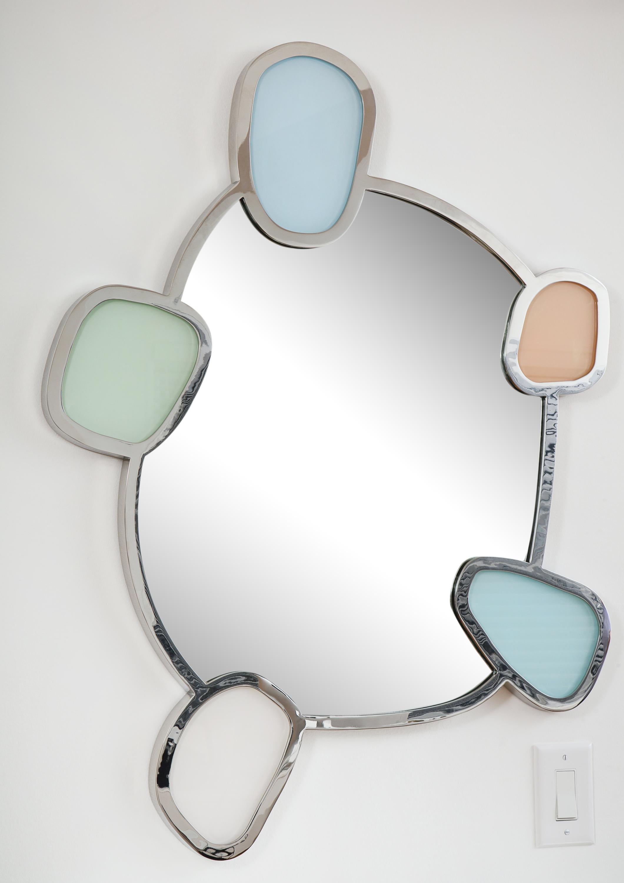 The biomorphic shaped mirror-plate within a conforming polished nickel surround inset with five colored-glass discs in pale blue, green, apricot, and white.