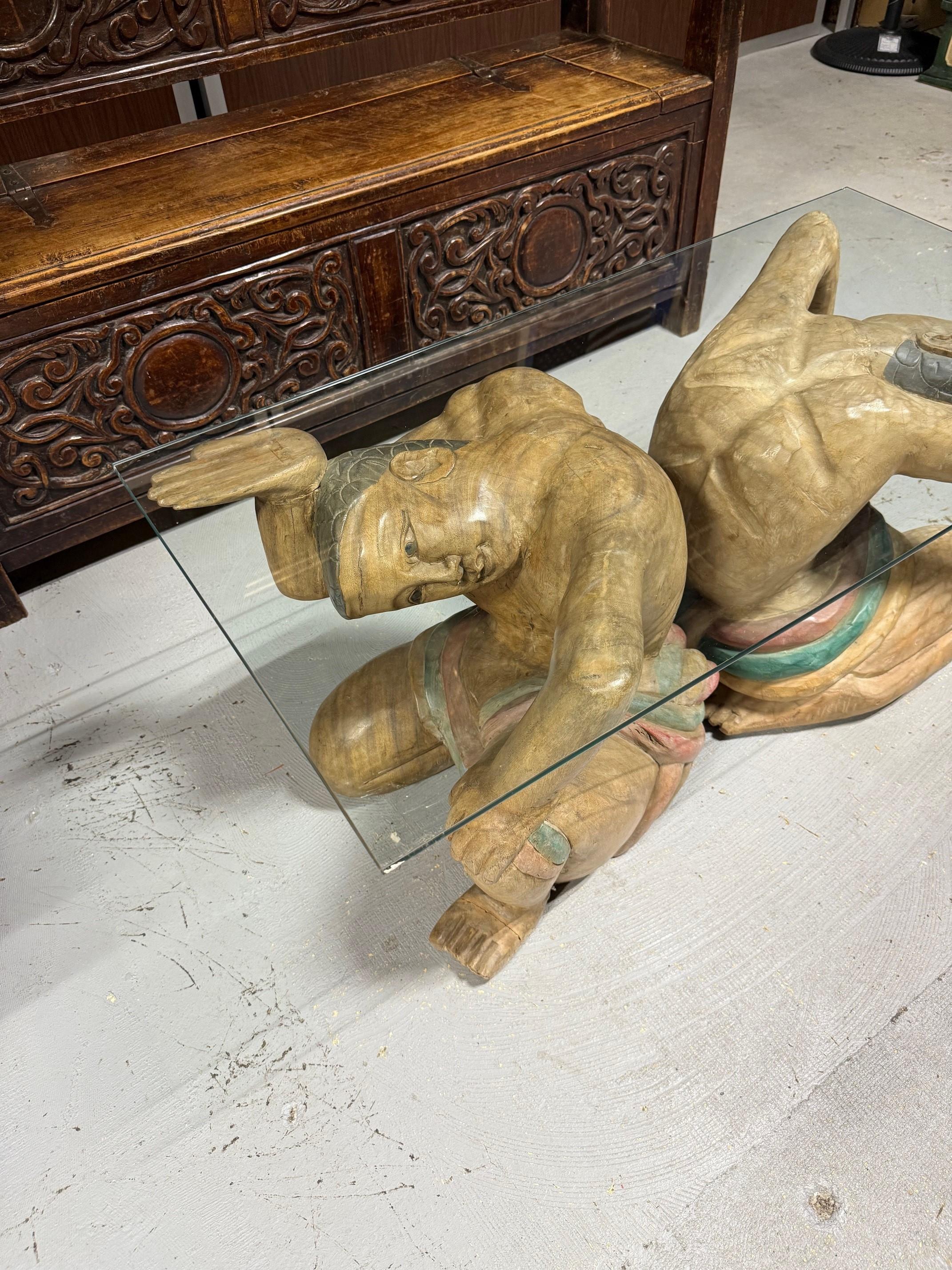 Amazing figural polychrome hand carved coffee table with a glass top. This is a great unique piece with two carved wood male figures holding a glass top. Overall in good condition but one foot is missing, shown in the photos. The two figures can be