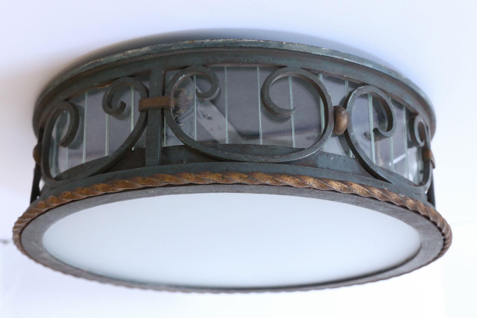 This flushmount fixture is in nice quality and has its original patina. The glass around the gallery was most probably added at some time and the frosted glass bottom is new glass. The light has been wired for the US. It has a classic style that