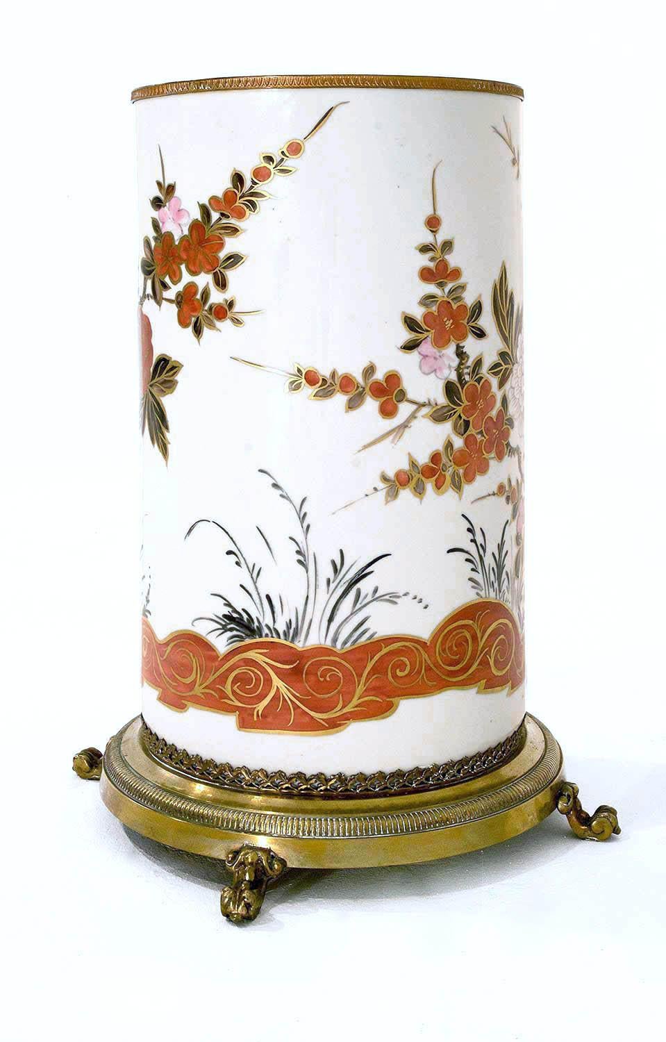 Cylindrical polychrome porcelain umbrella holder on a white background decorated with birds, leaves and branches, golden highlights, orange and rose peonies and flowers. Gilt bronze mount with a circular base, standing on three scrolled legs and
