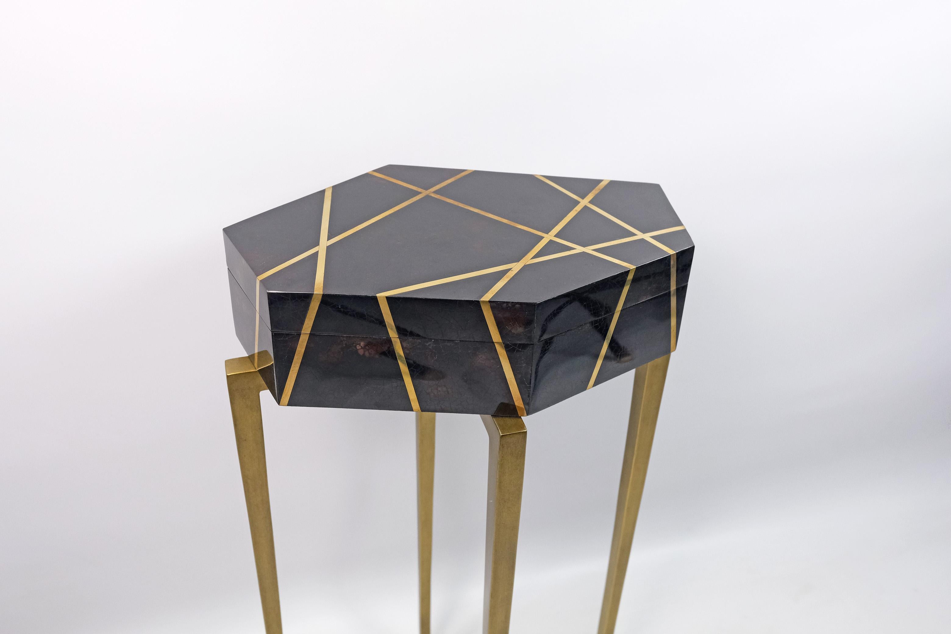 This futurist pedestal is made of polished black shell marquetry, with brass trims.

The top has a polygonal shape and you can open it to use it as box (for remote control or many other things). 
The metal feet have an antique brass patina.

The