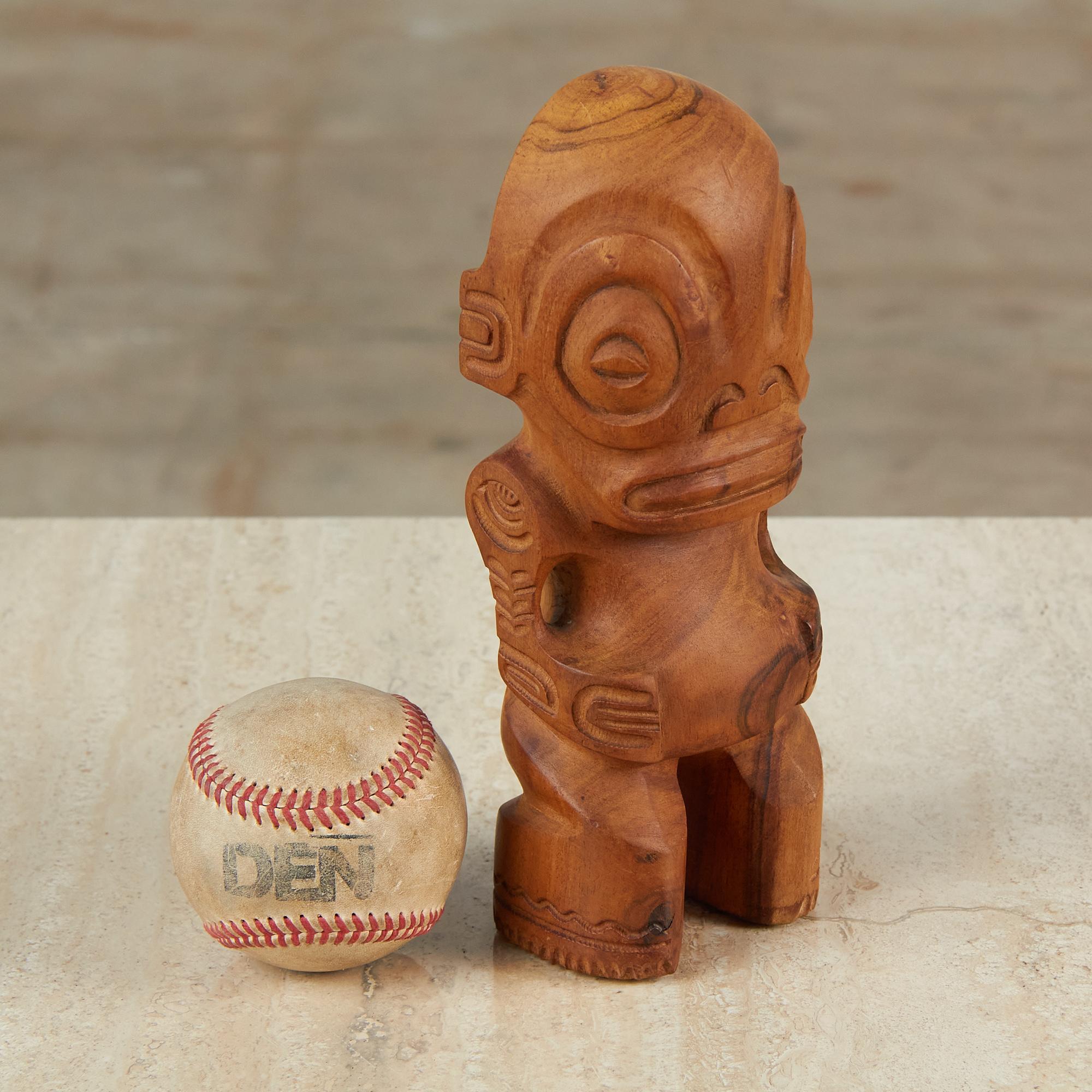 A small, hand-carved Polynesian sculpture from the Marquesas Islands with soft curved wood grain throughout. Carved from a solid piece of wood, this sculpture features large expressive eyes and mouth with intricate detailing on the outer arms and