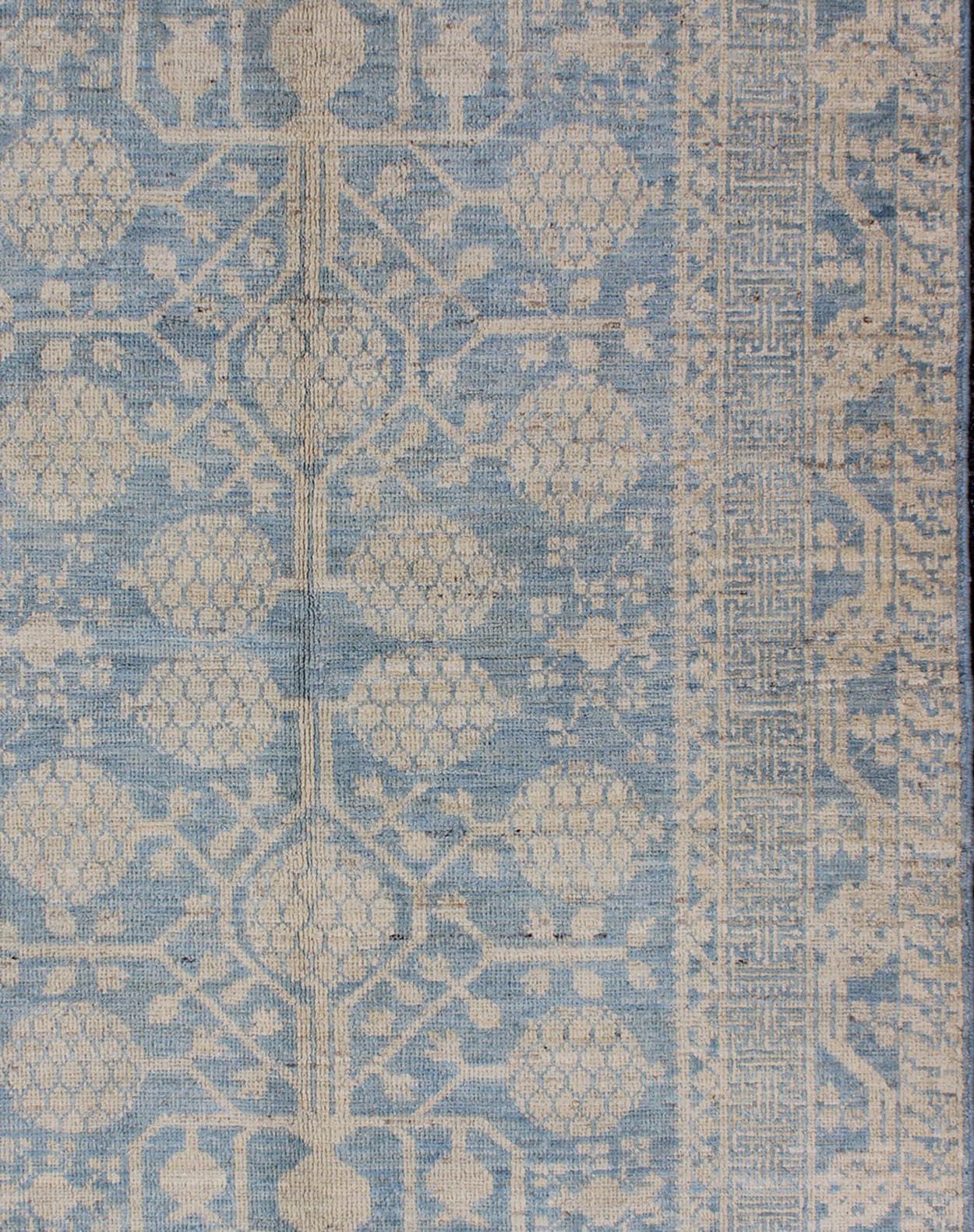 This Khotan features an all over Pomegranate Design flanked by a repeating pattern in the border. The entirety of the piece is rendered in light blue, and creams which makes it a versatile rug, well-suited for a variety of interiors including