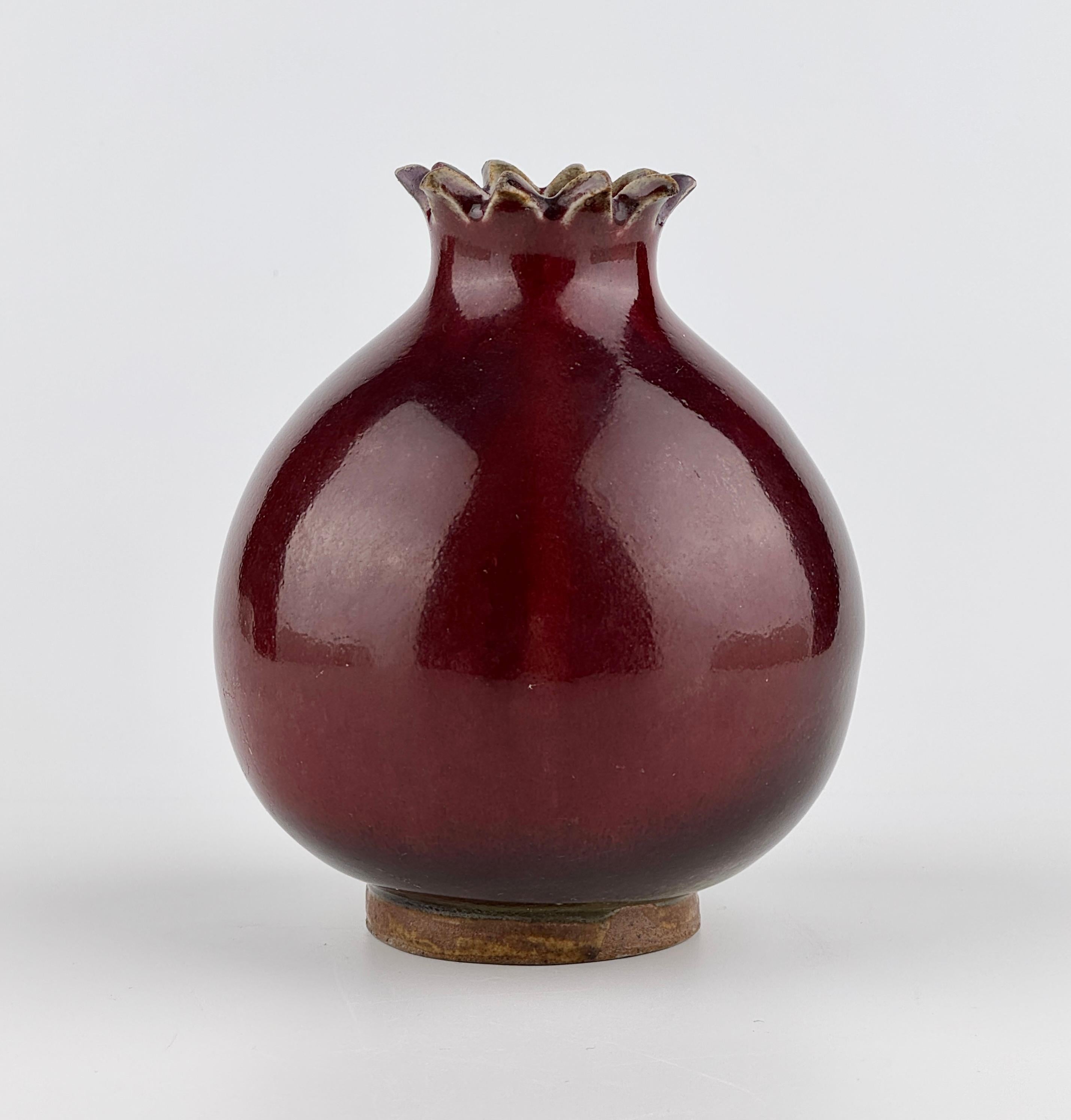 Questo pezzo è un piccolo vaso in ceramica con una silhouette distintiva modellata su un melograno, che si distingue per le sue curve piene e ben bilanciate. La bocca, che ricorda il calice del frutto, è resa con precisione, mentre l'intero corpo è
