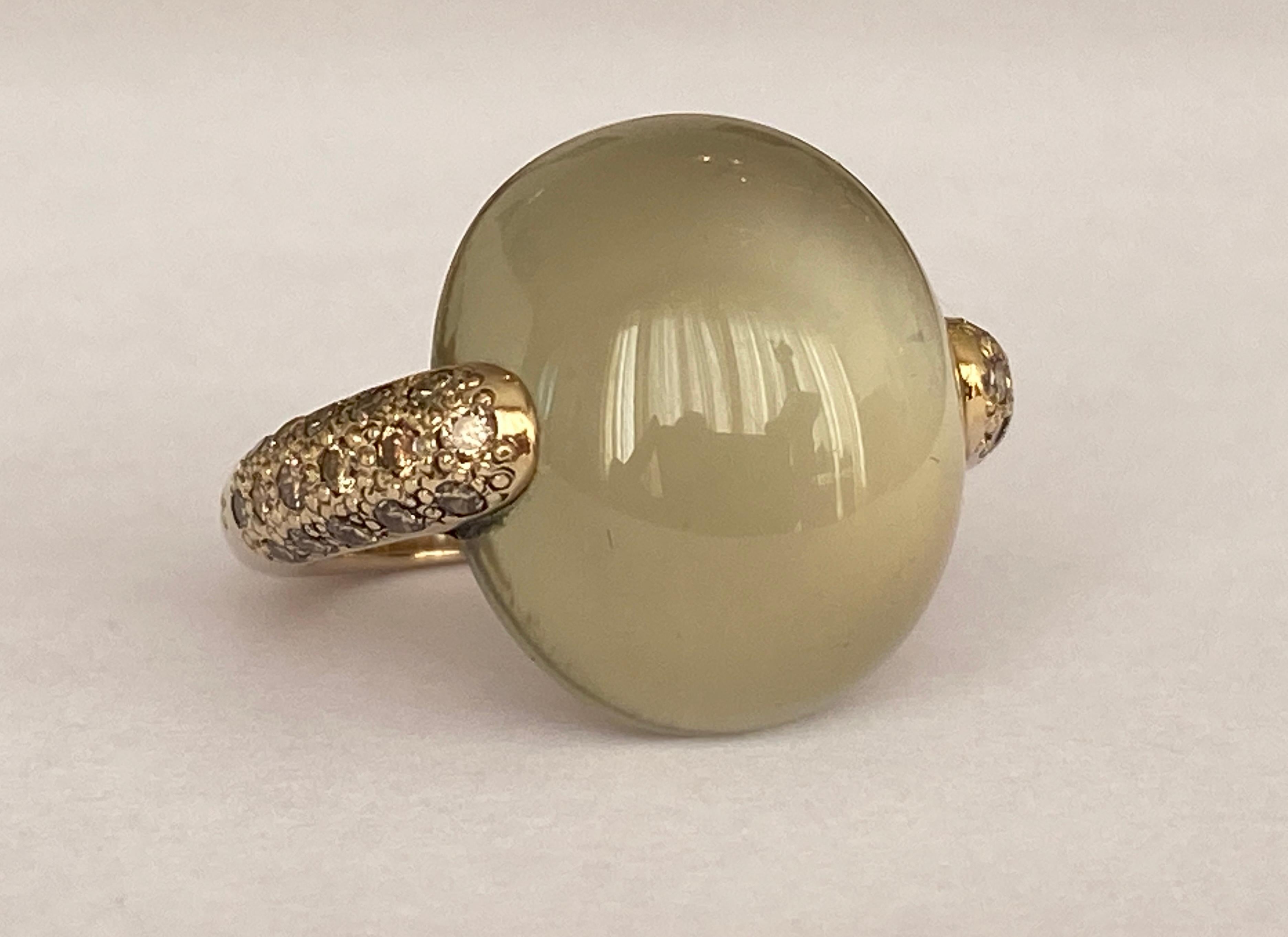 Ring, signiert von Maison Pomellato, Kollektion 'Luna', aus 750/000 natur  Gelbgold mit einem Mondstein-Cabochon in der Mitte und 32 cognacfarbenen Diamanten (ca. 0,66 ct) in der Mitte.
Höhe: 19 mm
Fingergröße: 51 (aber auch für Größe 52