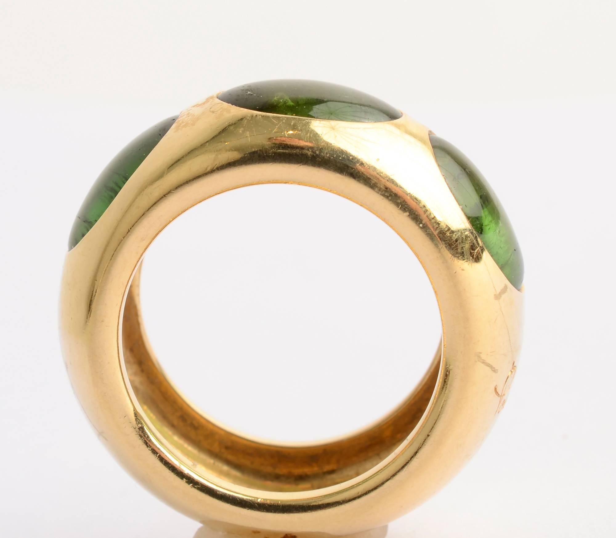 Substantial 18 karat gold ring by Pomellato with three green tourmaline stones. The ring is 7/16 inch tall all around. 
What may initially appear to be scratches are actually the Pomellato logo written on the outside of the ring. There are, however,