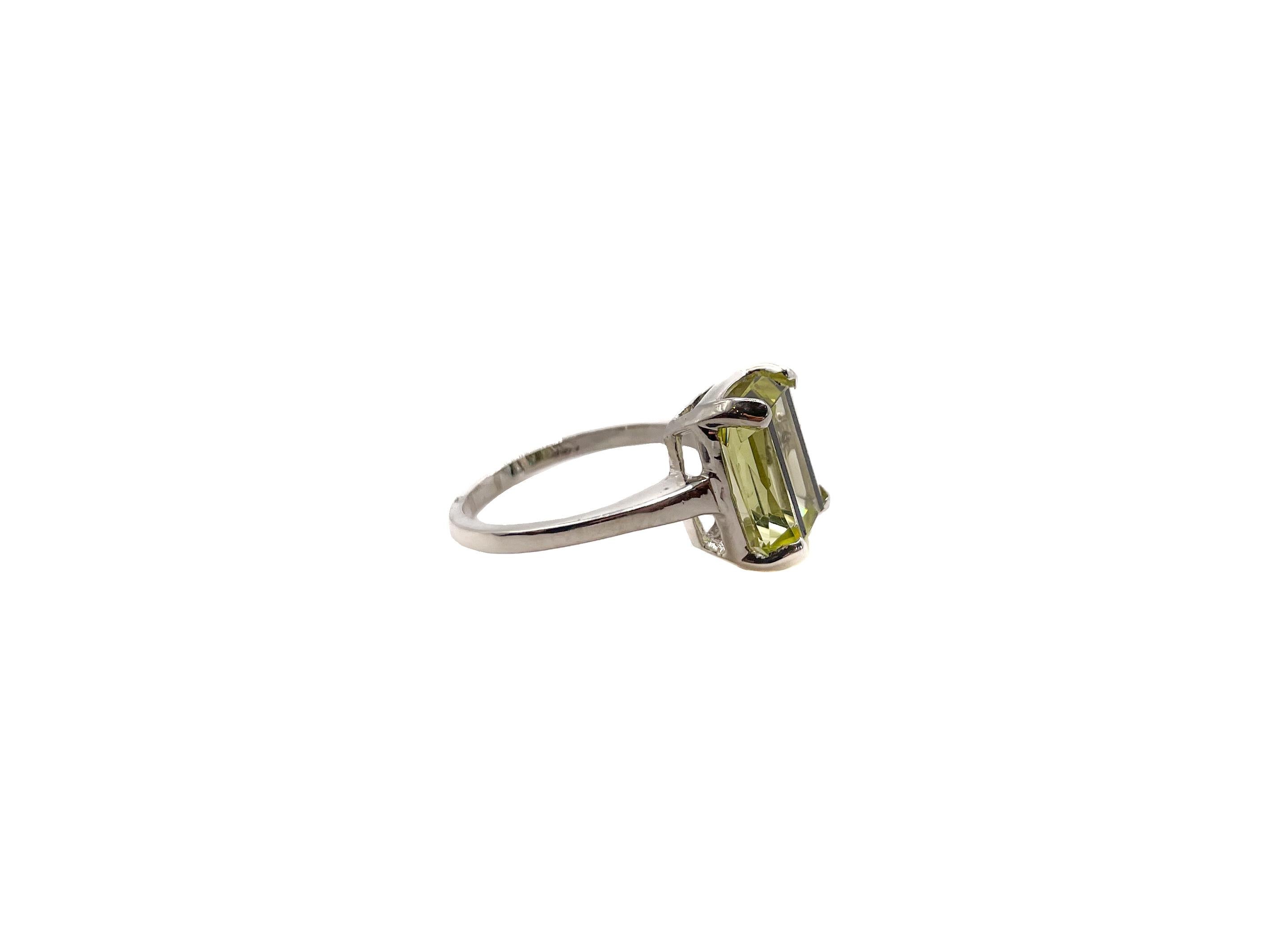 This elegant cocktail ring has the unique appearance of being marked by two parallel black lines that run through the glass stone. The strong geometrical motif showcases the clean symmetry of Art Deco style. 

The stone is made from beveled emerald
