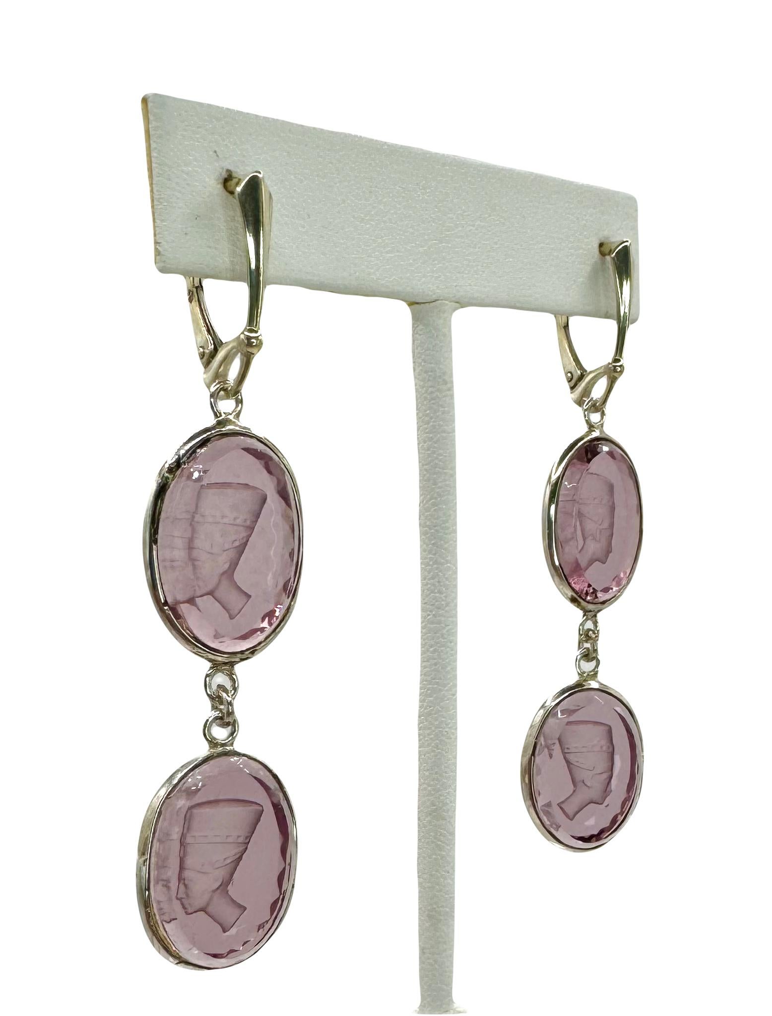 These Egyptian Revival earrings are intaglios of Queen Nefertiti's profile. The cabochons are made from light amethyst glass from 1950s Czech Republic. The earrings are set in sterling silver and hang from Egyptian style lever-back ear