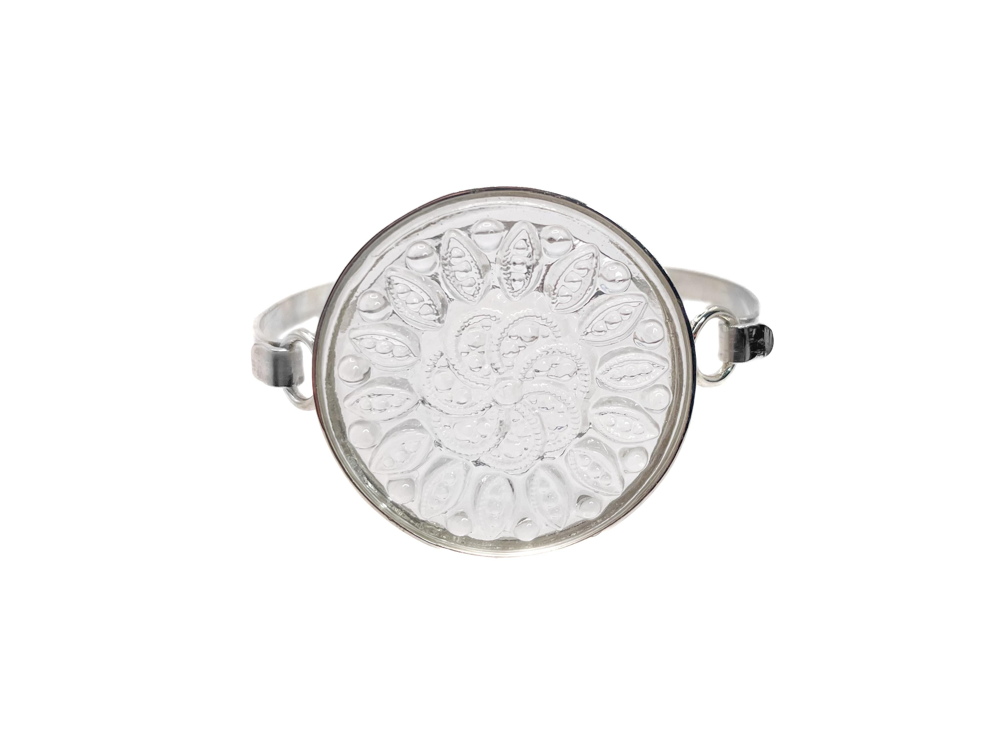 This timeless bracelet, in the style of Lalique, showcases a clear Camellia floral motif glass cabochon from Germany. 

The round molded piece of glass is set in a NEW modern sterling silver setting. It has an elegant and effortless hook clasp. The