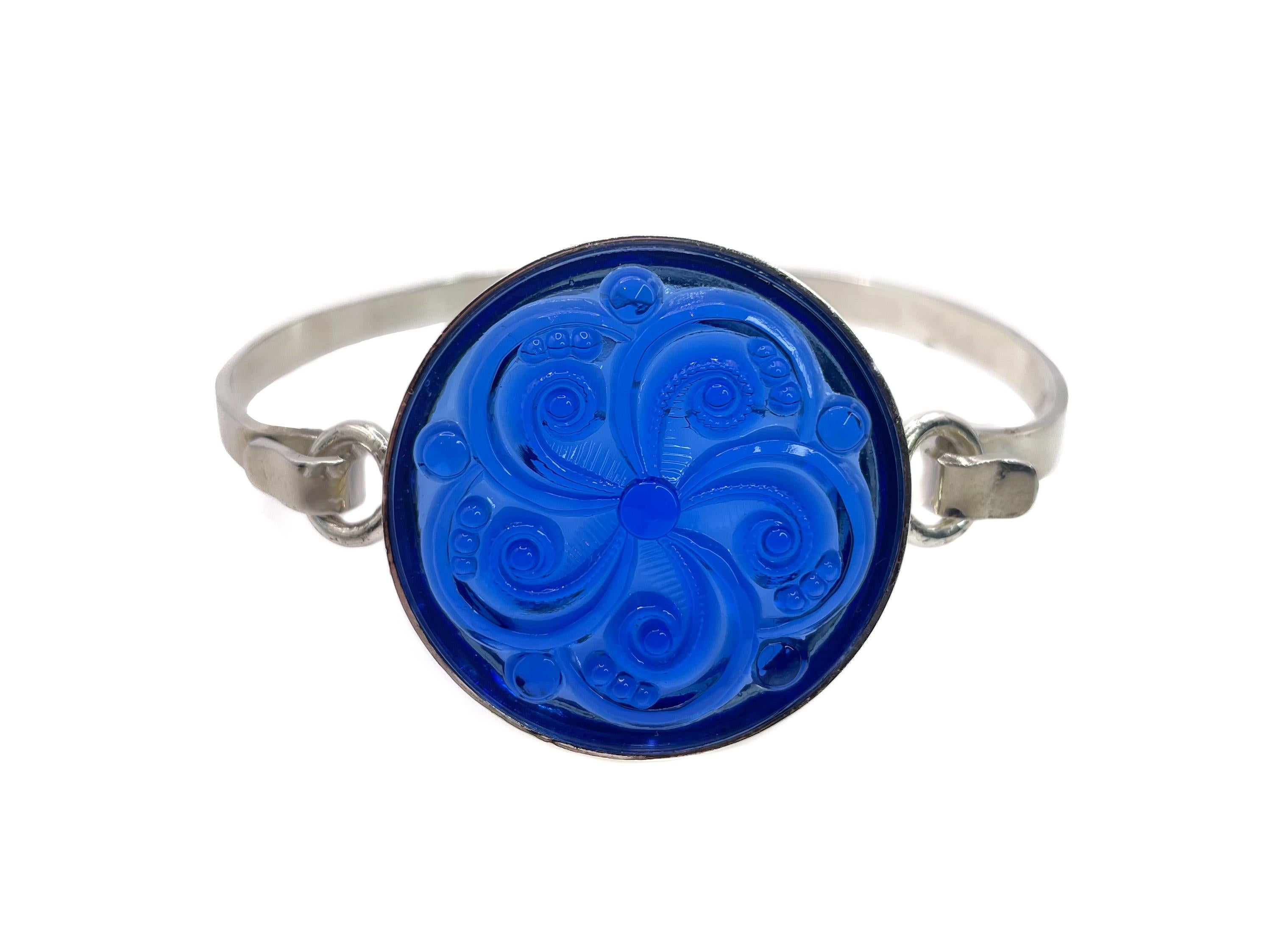This refined bracelet, in the style of Lalique, showcases a sapphire swirl motif glass cabochon from Germany. 

The round molded piece of glass is set in a NEW sterling silver setting. It has an elegant and effortless hook clasp. The glass stone
