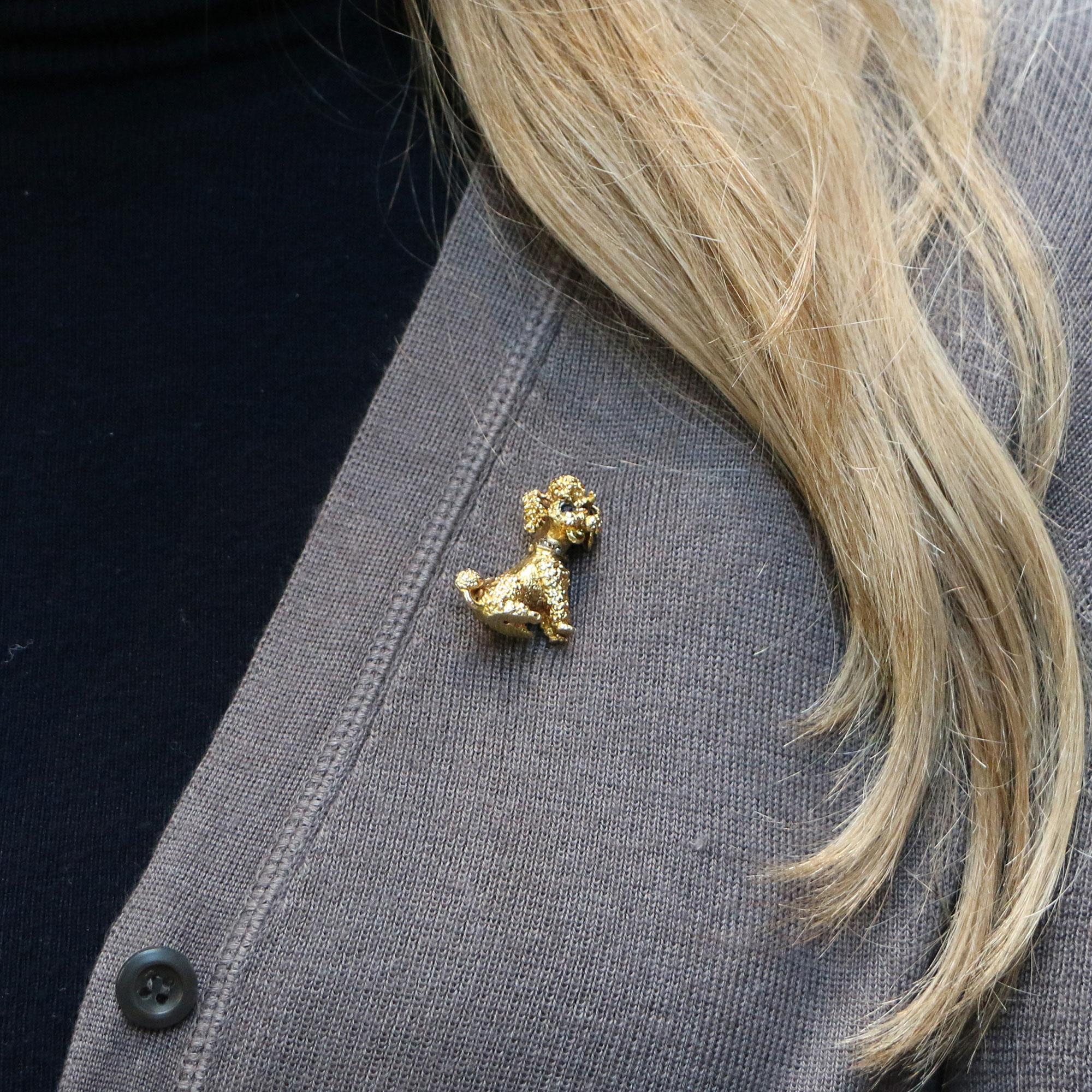 A delightful yellow gold poodle brooch  This useful brooch is exquisitely hand crafted in 9K yellow gold and features textured gold fur, a sparkling collar studded with rose cut diamonds and piercing blue sapphire eyes. It is very easy to wear