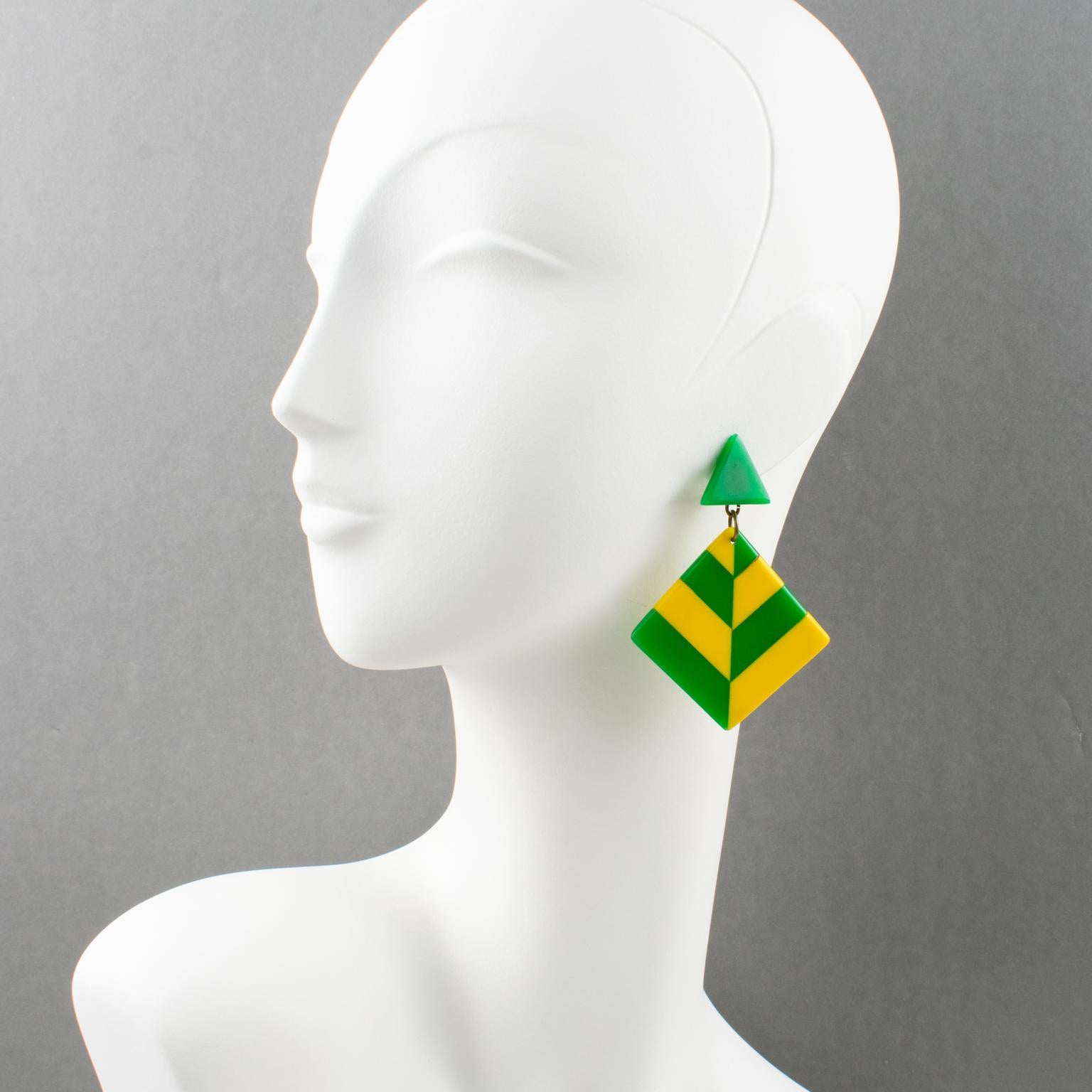 These stunning 1960s Pop Art Bakelite dangling clip-on earrings feature a geometric dangling shape with a square laminated design in a checkerboard pattern. The pieces have lovely green grass, bright yellow colors, and French clipbacks. There is no
