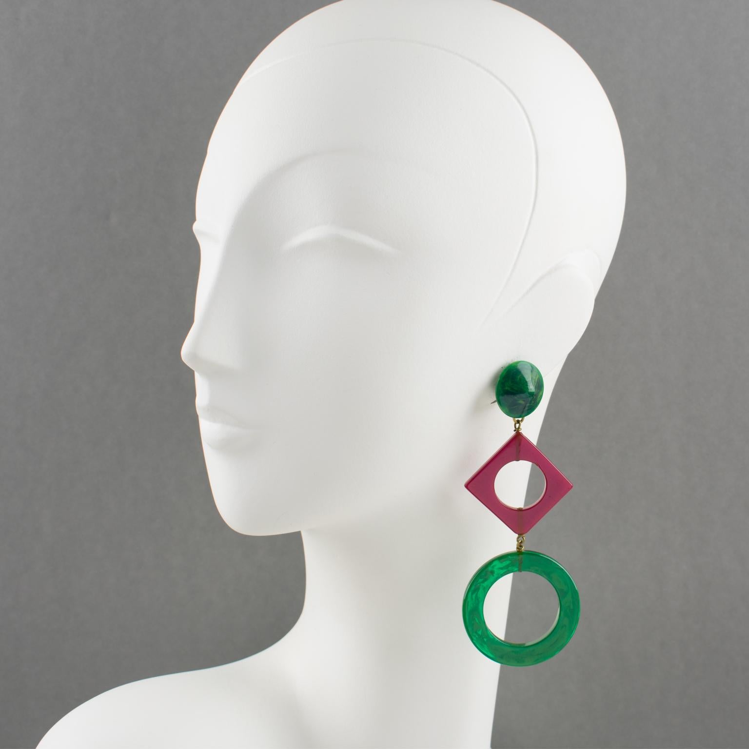 These stunning extra-long Bakelite dangling clip-on earrings have an undeniable Pop Art design flair. They feature a chandelier shape with a geometric design using square donuts and large ring forms in blue-moon green marble and purple plum colors.