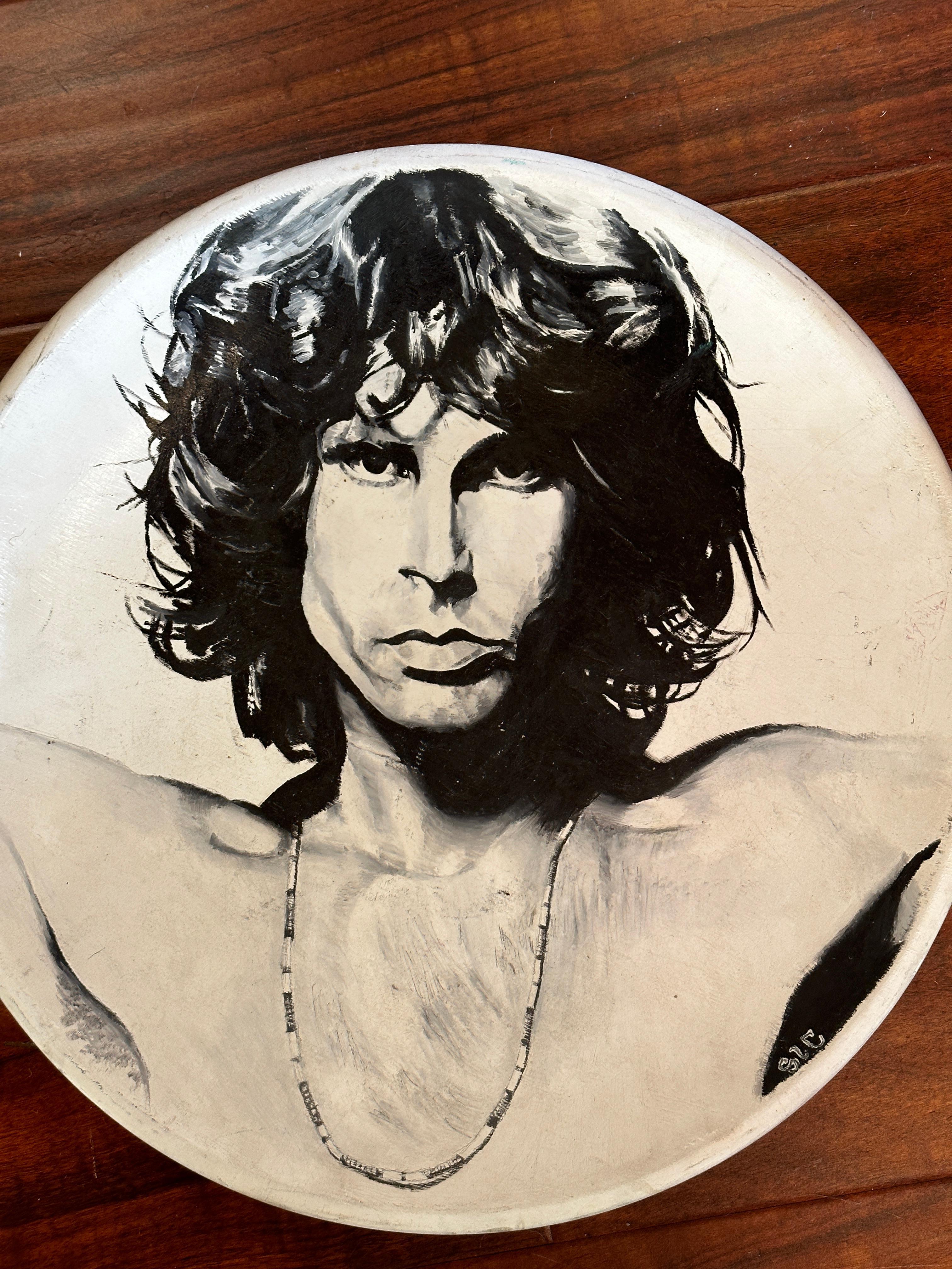 Cette assiette en céramique peinte à l'acrylique présente une reproduction de l'un des portraits emblématiques de Jim Morrison réalisés par le photographe Joel Brodsky. L'artiste représente les traits frappants de Morrison fidèles à la photo