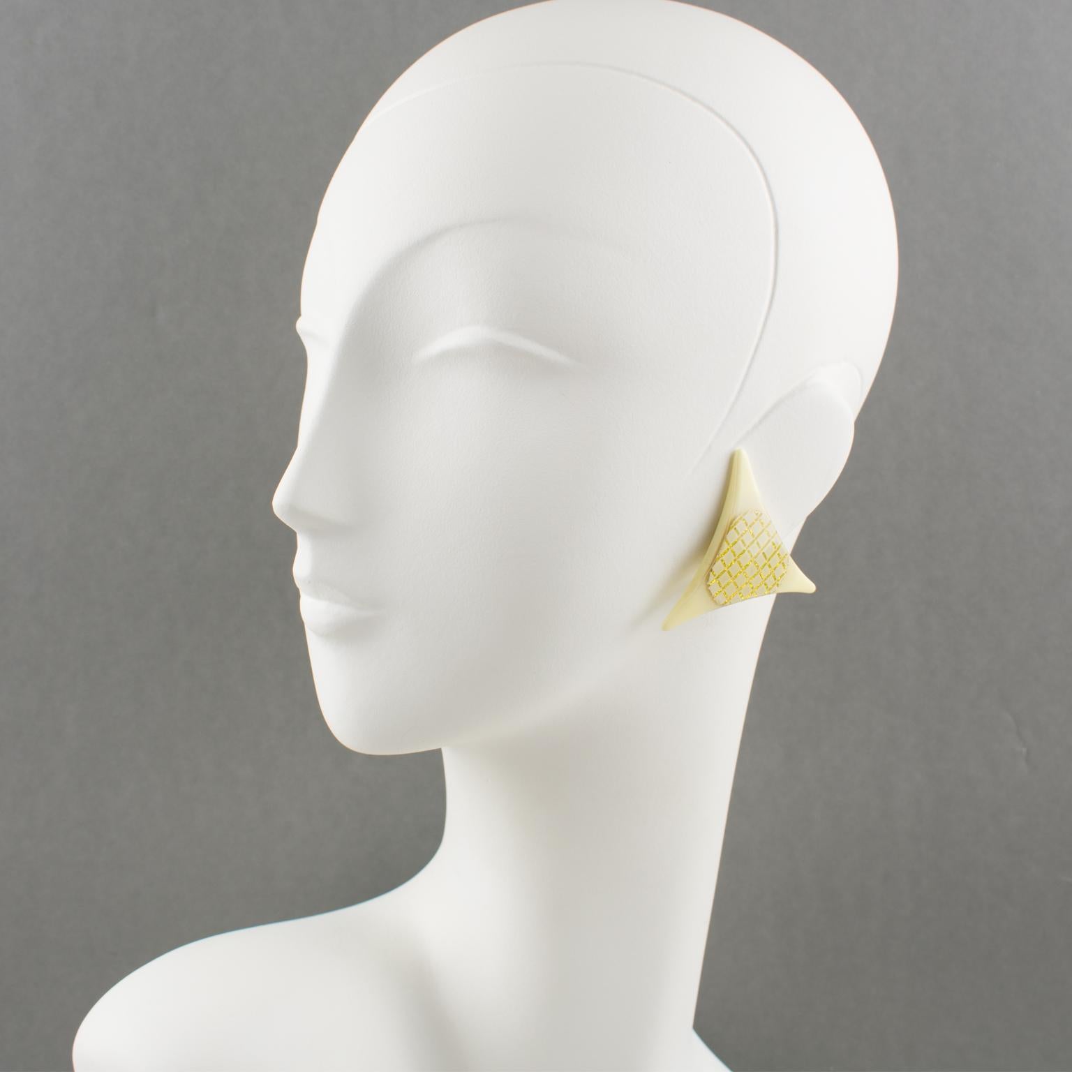 These charming French Artisan Studio Lucite clip-on earrings feature a typical Pop Art design with a large triangle shape and textured pattern. The assorted tone of ivory/cream-white is embellished with gilt plaiting. There is no visible maker's