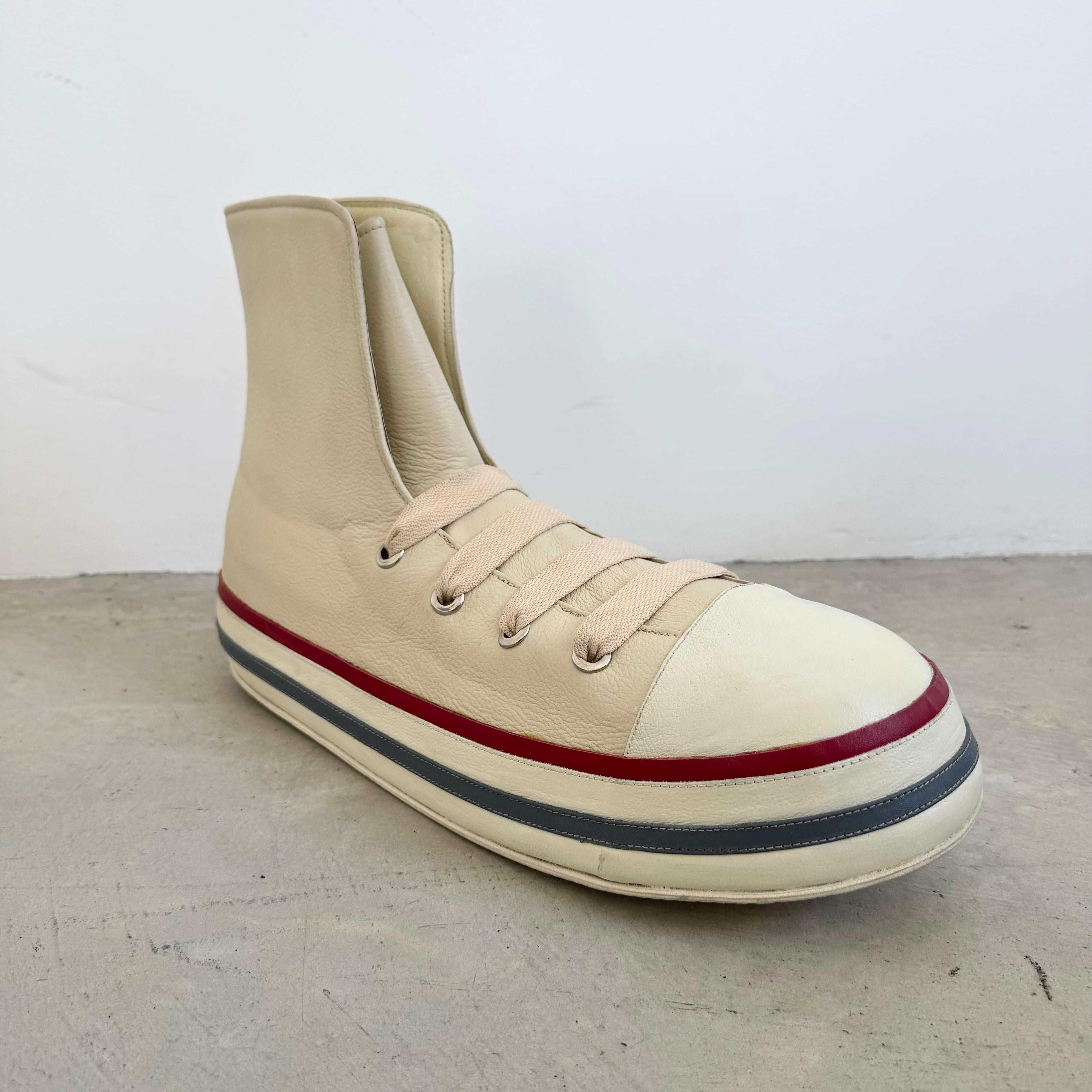 Questa sneaker oversize di grande impatto, realizzata in morbida pelle color crema, è un pezzo scultoreo che confonde in modo giocoso il confine tra moda e arte. Ispirato alla sensibilità della Pop Art, esagera la forma familiare di una classica
