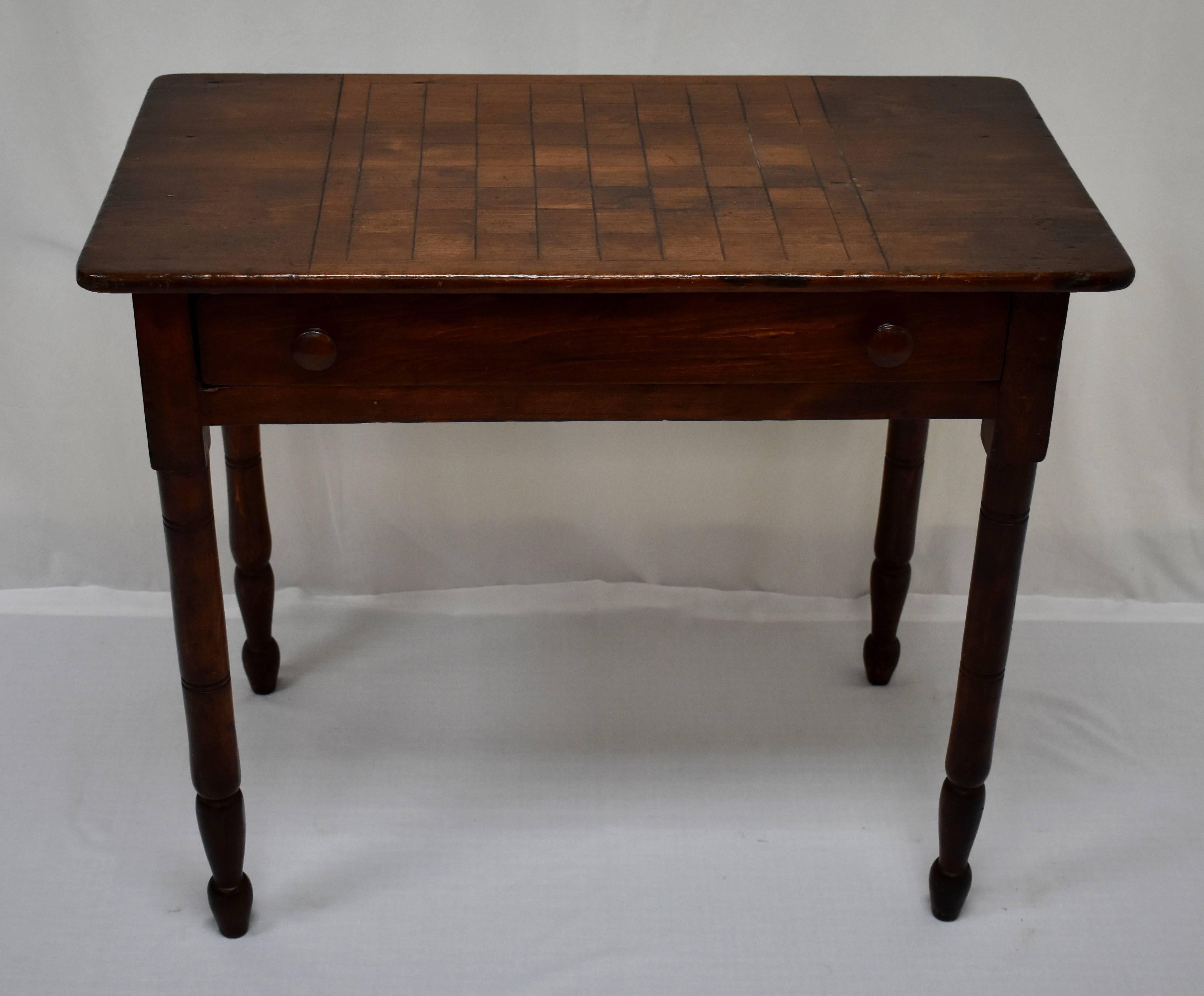 This attractive American poplar side table has four slender turned and incised legs and a single long peg-joined drawer with original wooden knobs. A 64 square game board with border is etched into the top and the piece is finished in a rich walnut