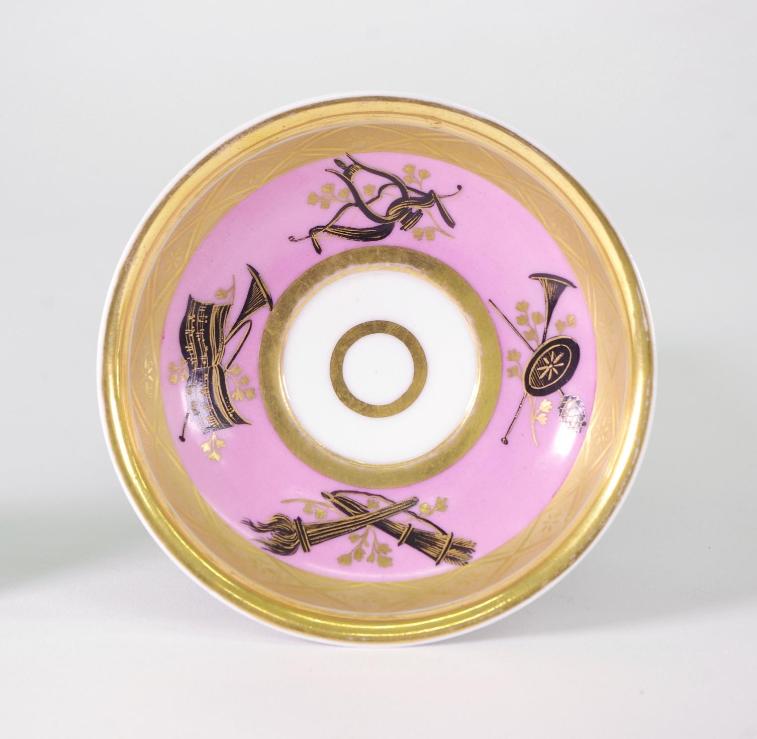 Popov cup and saucer, each piece with pink enamel ground, decorated in black with neoclassical devices and further embellished with Fine gilt borders, the handle with an impressed flower motif. Underglaze blue mark to the cup; impressed mark to the