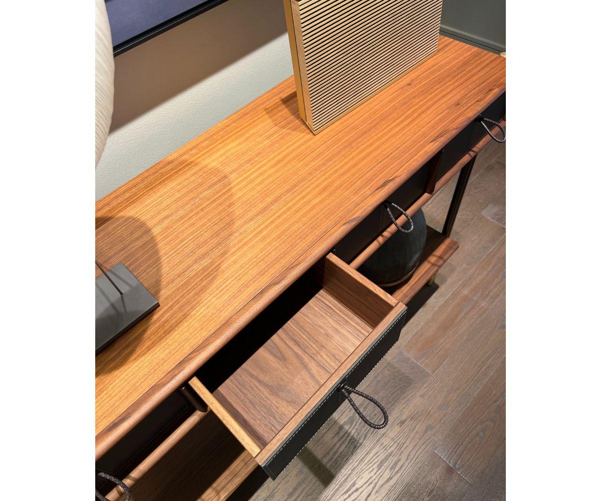 The Porada Console, designed by Gabriele & Oscar Buratti, is a stunning piece crafted in Canaletto walnut with four drawers featuring leather details. The top and compartment dividers are made from solid Canaletto walnut, providing a seamless and