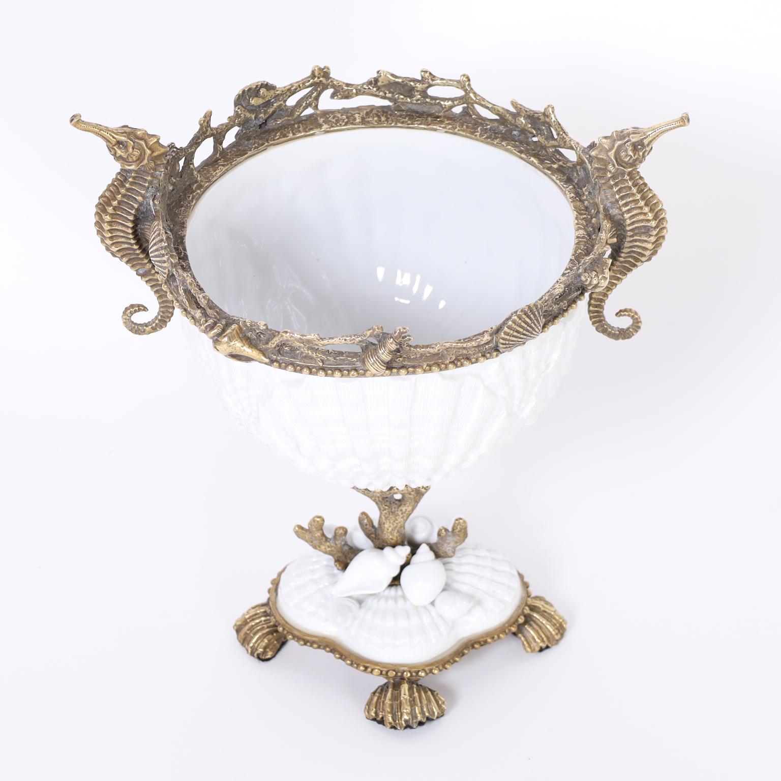 Sea inspired compote with a white glazed porcelain bowl decorated with brass seashells and seahorses supported by a brass coral stem on a base with porcelain seashells and brass shell feet.