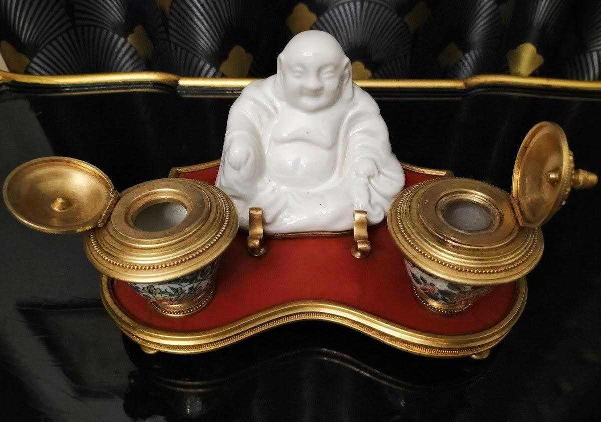 Porcelain and bronze inkwell in the taste of Asian Art.

Inkwell decorated with a Buddha in white porcelain on a red lacquer tray mounted with gilt bronze and inkwells in porcelain and gilt bronze, Napoleon III style, early 20th century, minor
